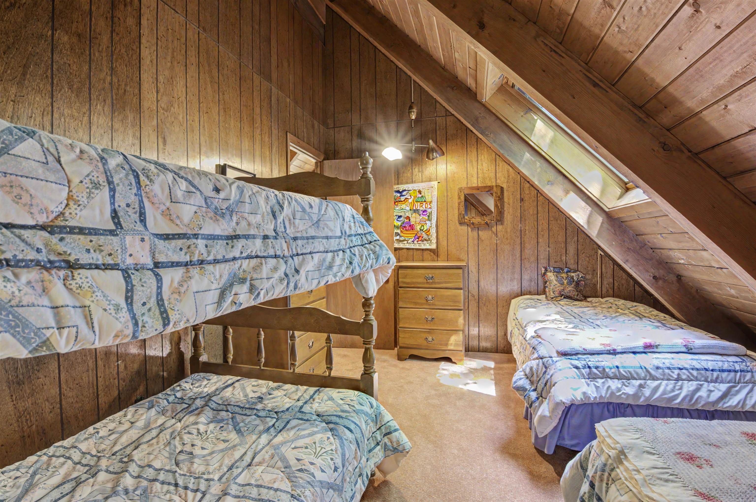 Attic bedroom with multiple quilt-covered beds, wood-paneled walls, and a skylight.