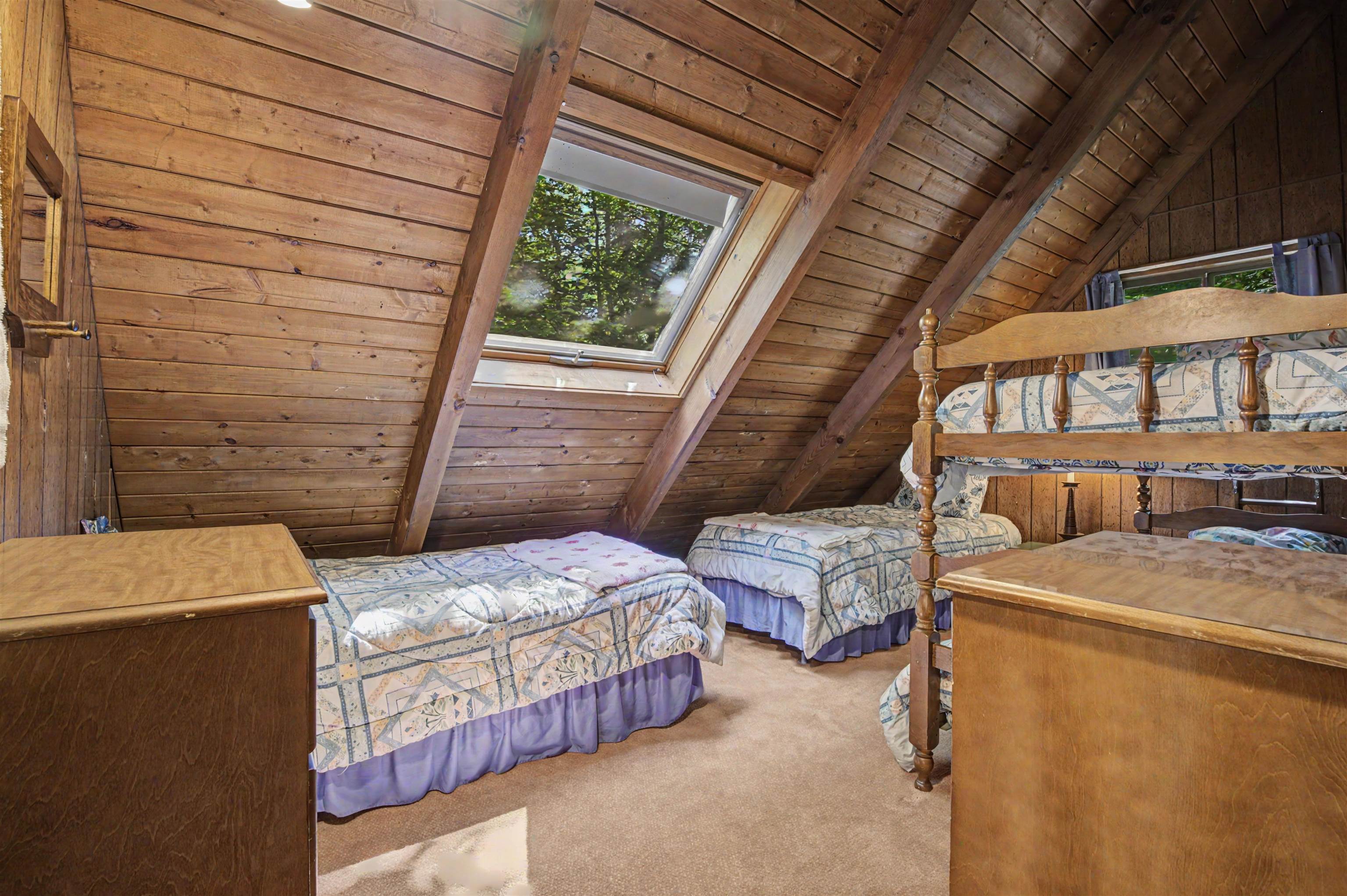 Attic bedroom with several beds beneath a skylight and exposed wooden beams.