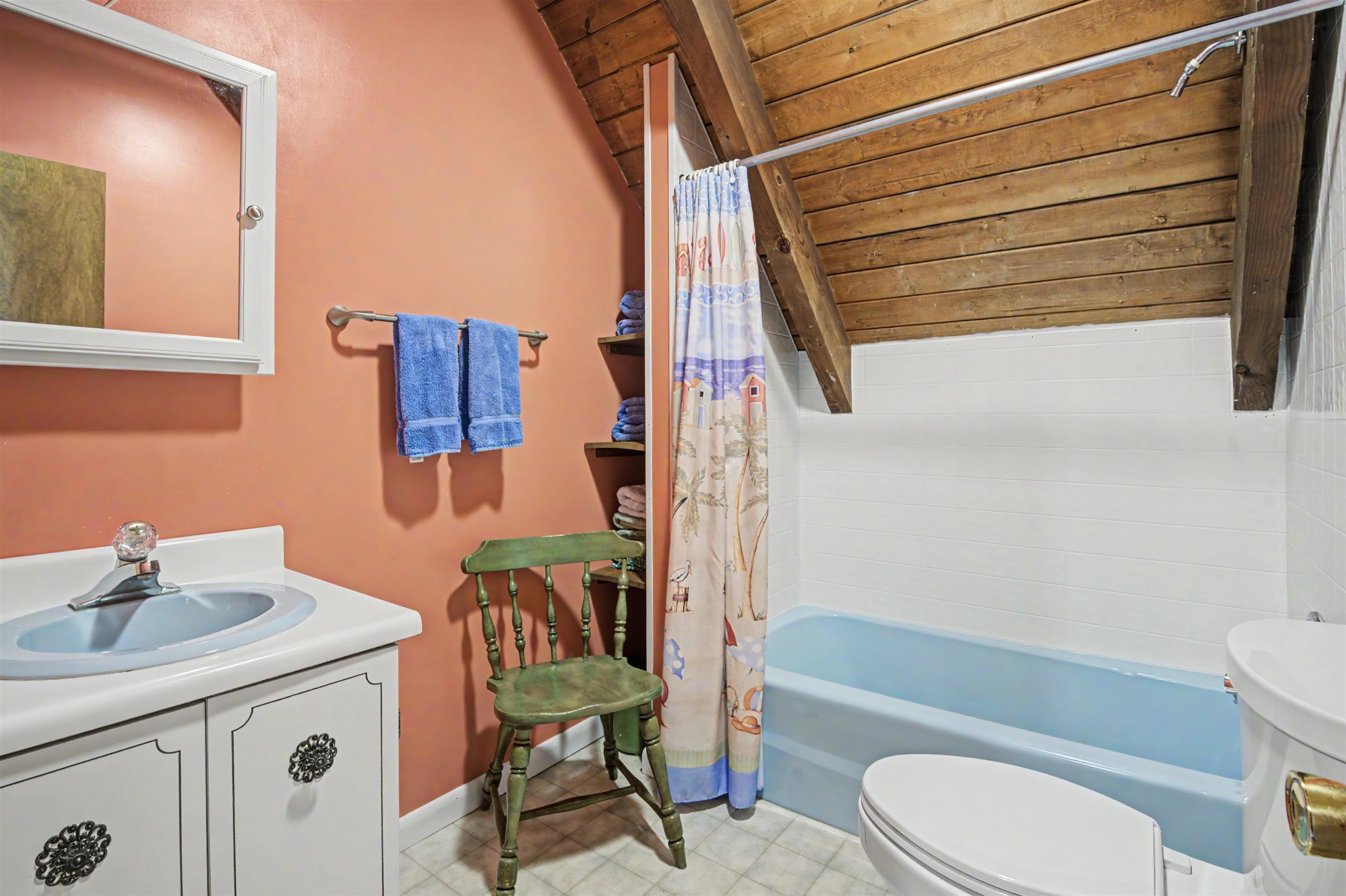 Bathroom with a blue bathtub beneath a sloped exposed-wood ceiling and a salmon-colored wall.