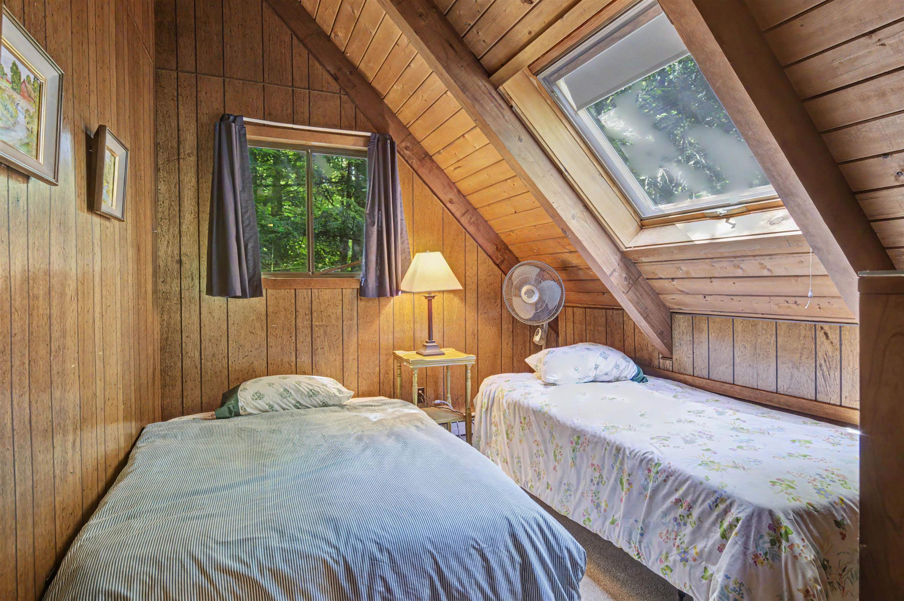 Attic bedroom with two beds, wood-paneled walls, exposed beams, and a large skylight.