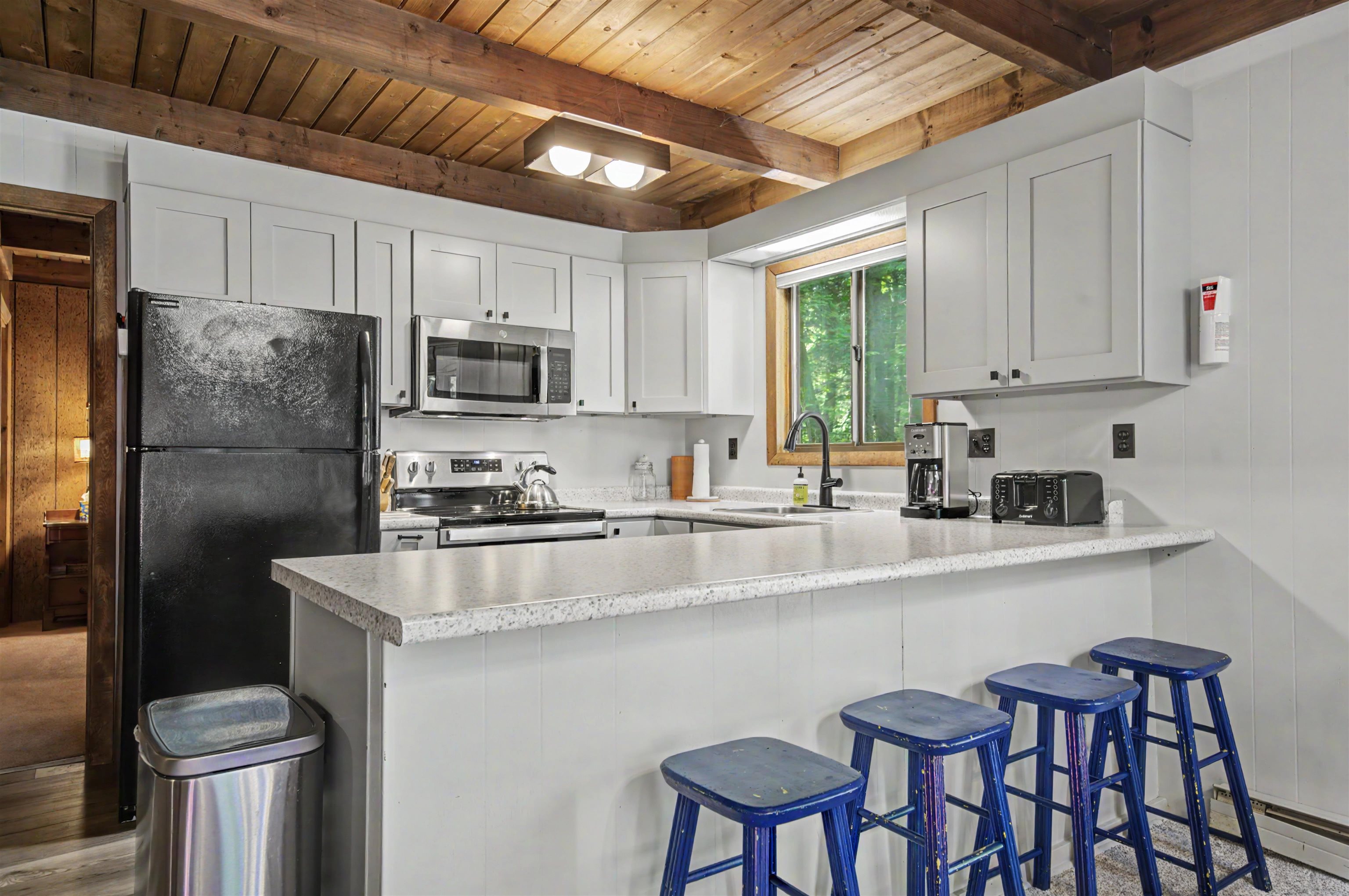 Kitchen with a speckled countertop peninsula, blue stools, white cabinets, and a rustic wood ceiling.
