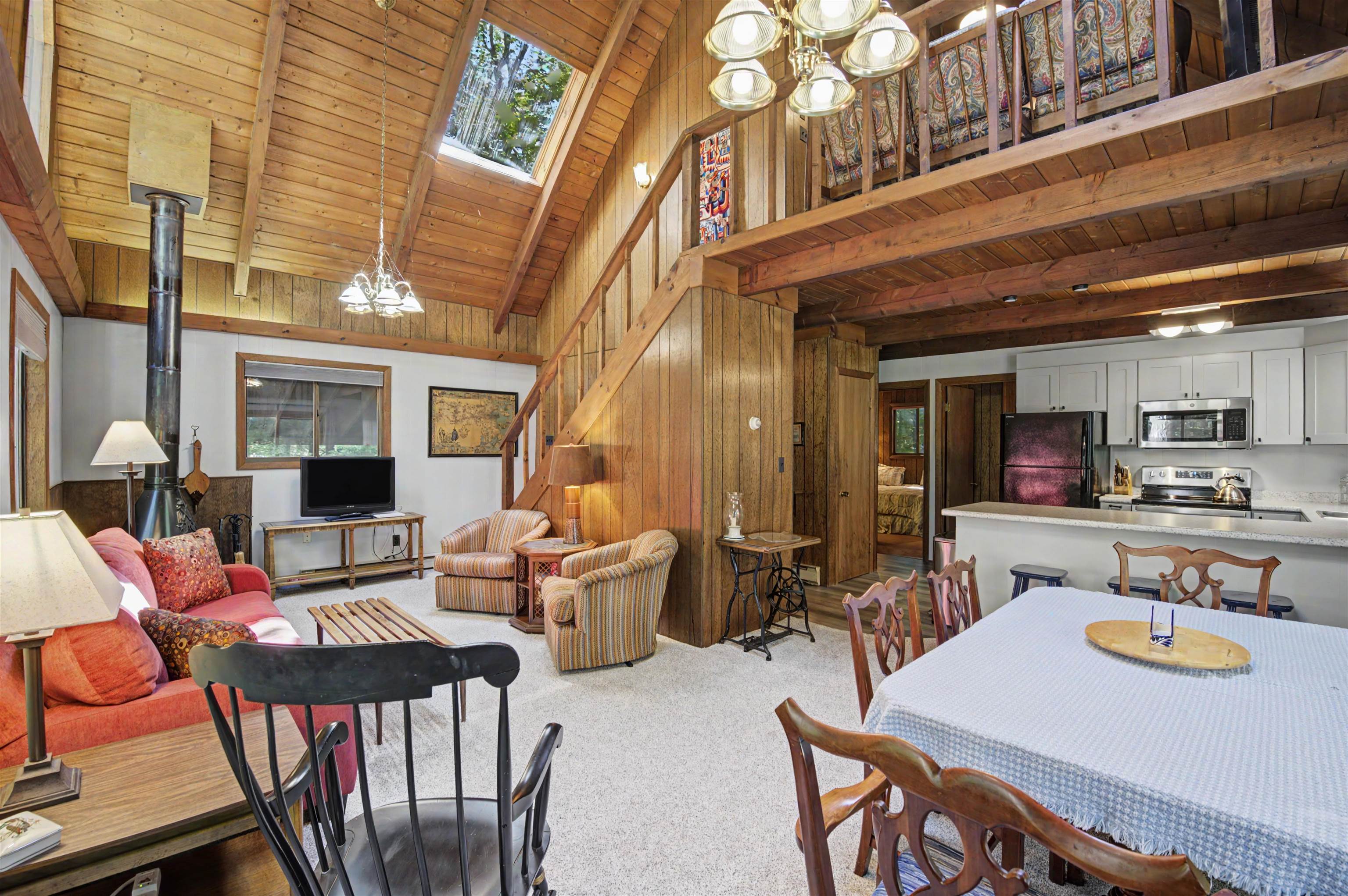 Open-plan living and dining area with a vaulted wood ceiling, loft, skylight, and adjoining kitchen.