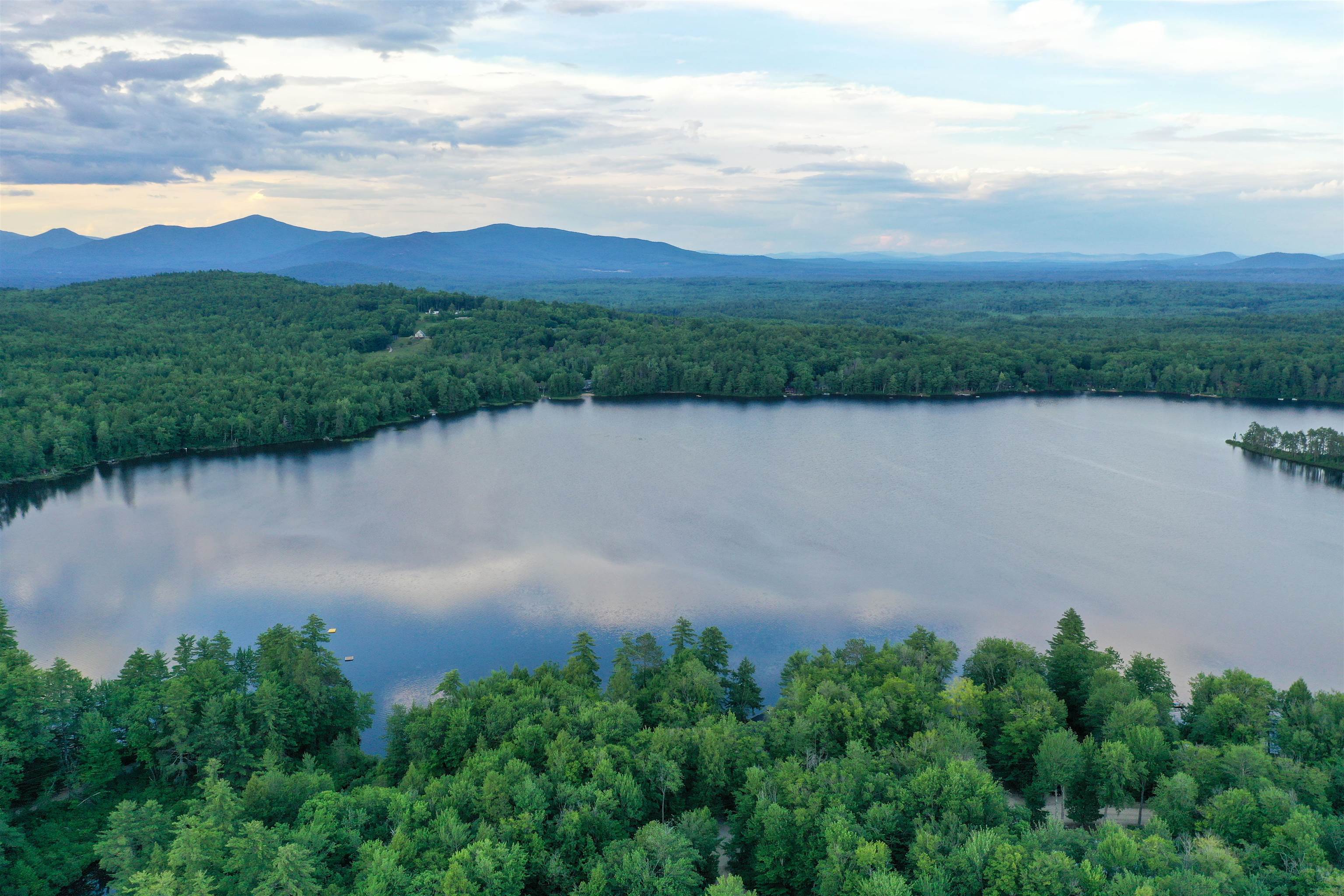 Aerial view of a forest-lined lake with distant mountains beyond.