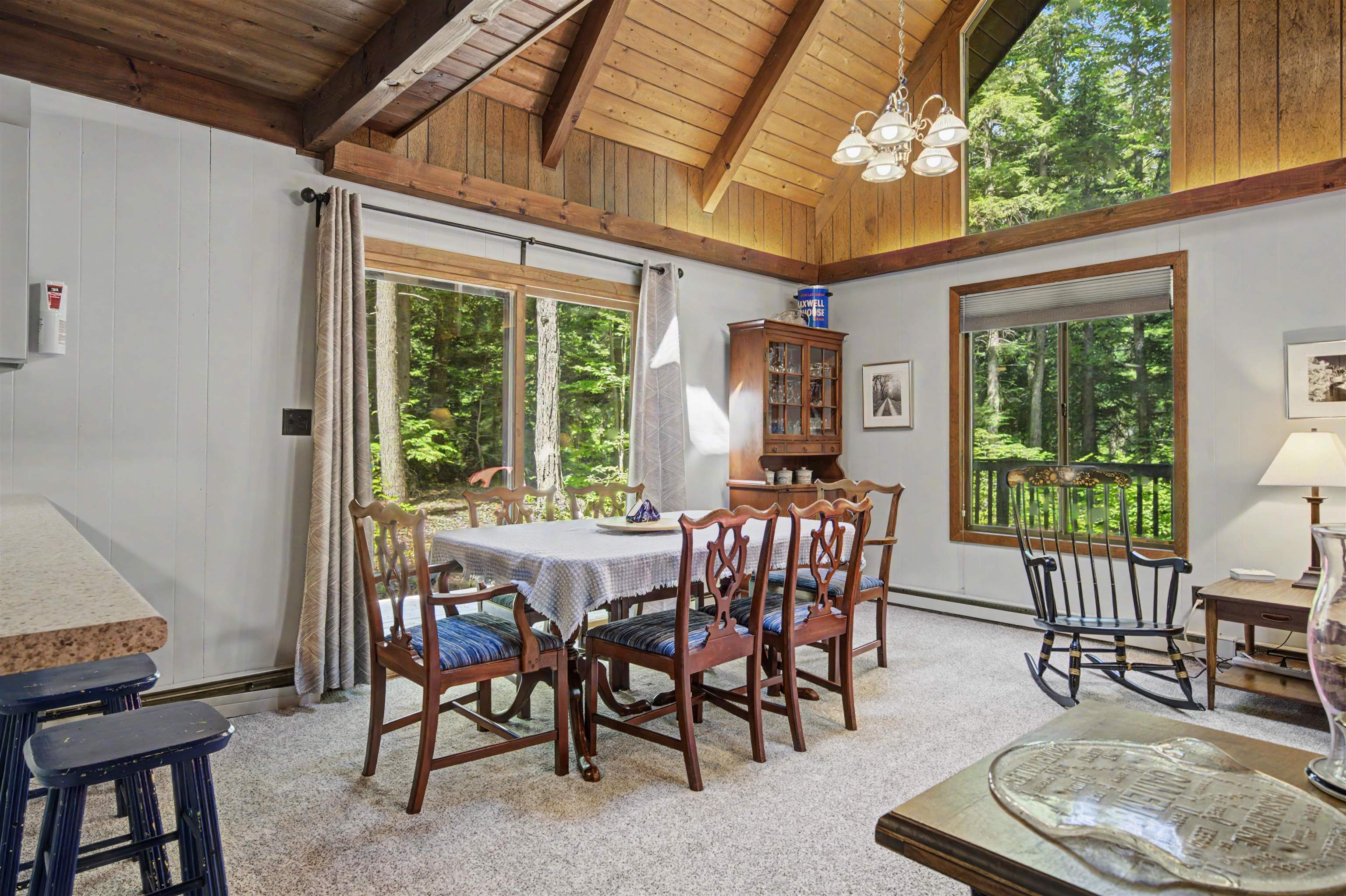 Dining room with a vaulted wood ceiling, wooden dining set, and windows overlooking the woods.