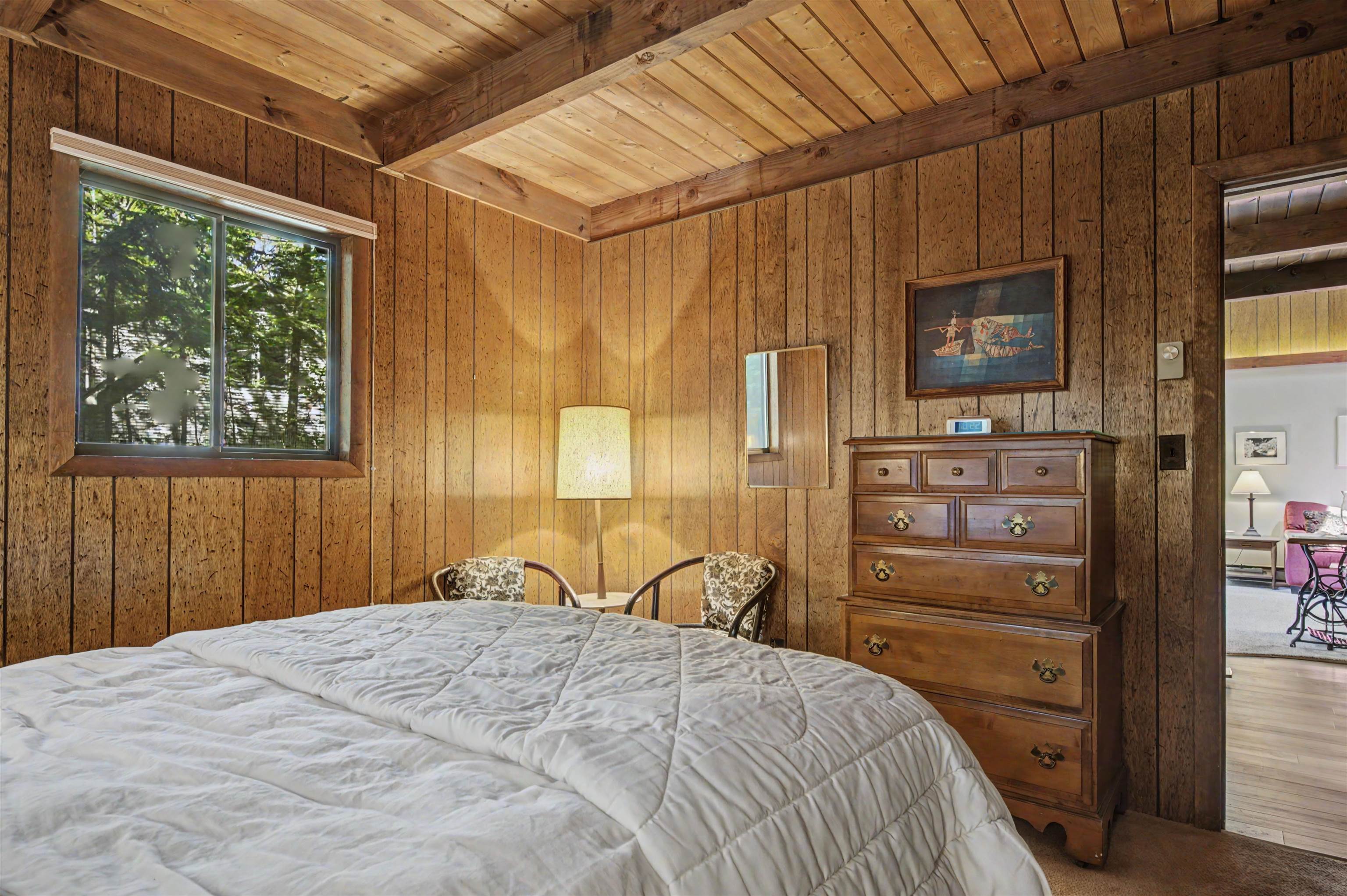 Bedroom with a wood-paneled vaulted ceiling, large bed, and tall dresser.