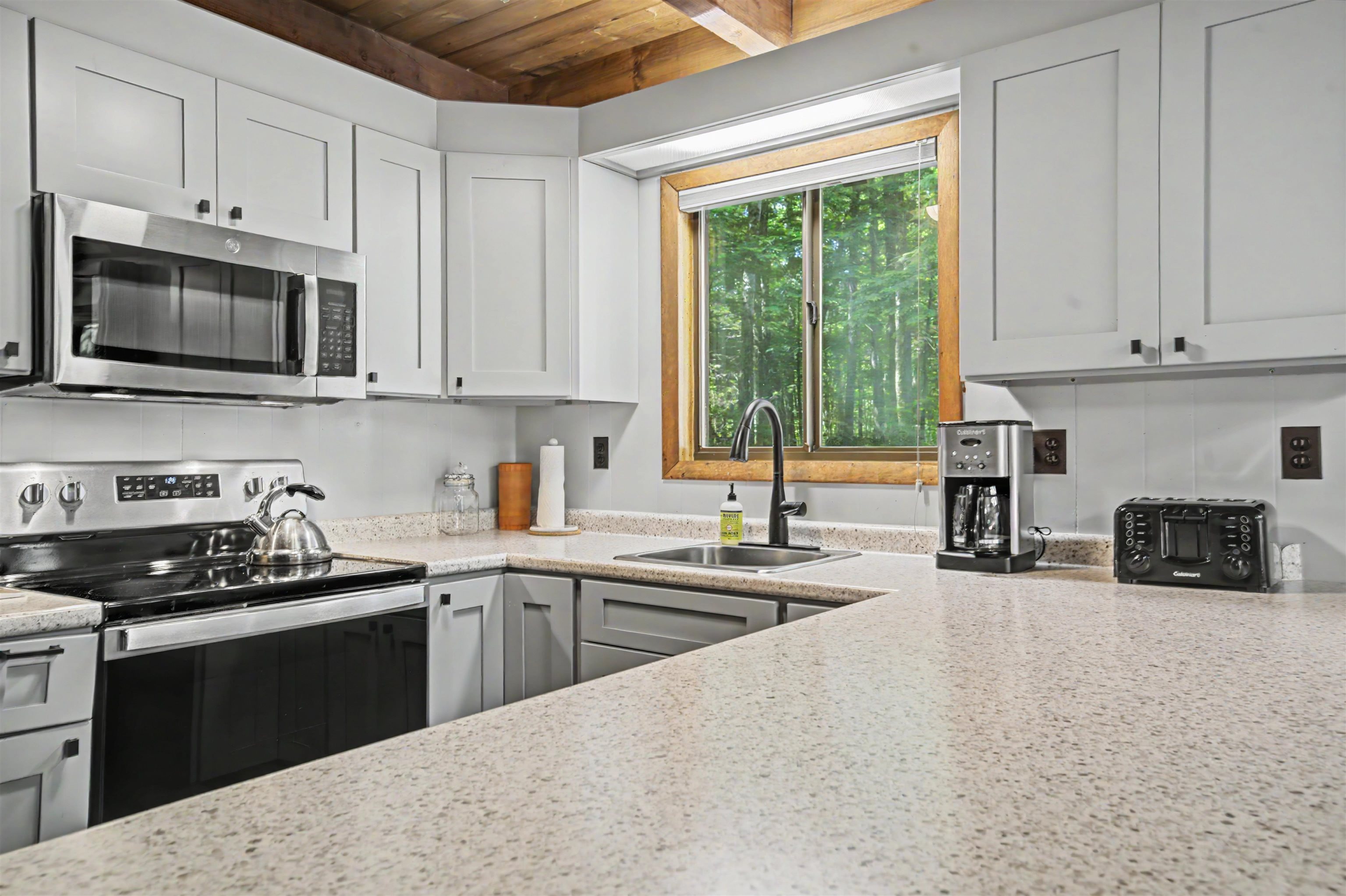 Kitchen with white cabinets, stainless appliances, and a sink beneath a window overlooking trees.