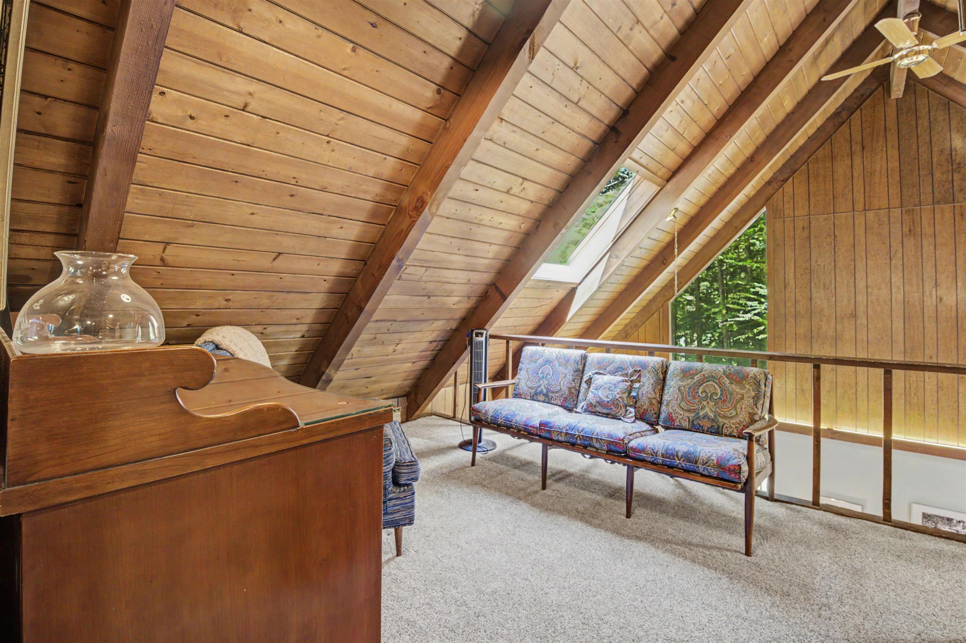 Attic sitting area with exposed timber ceiling, skylight, and patterned sofa.
