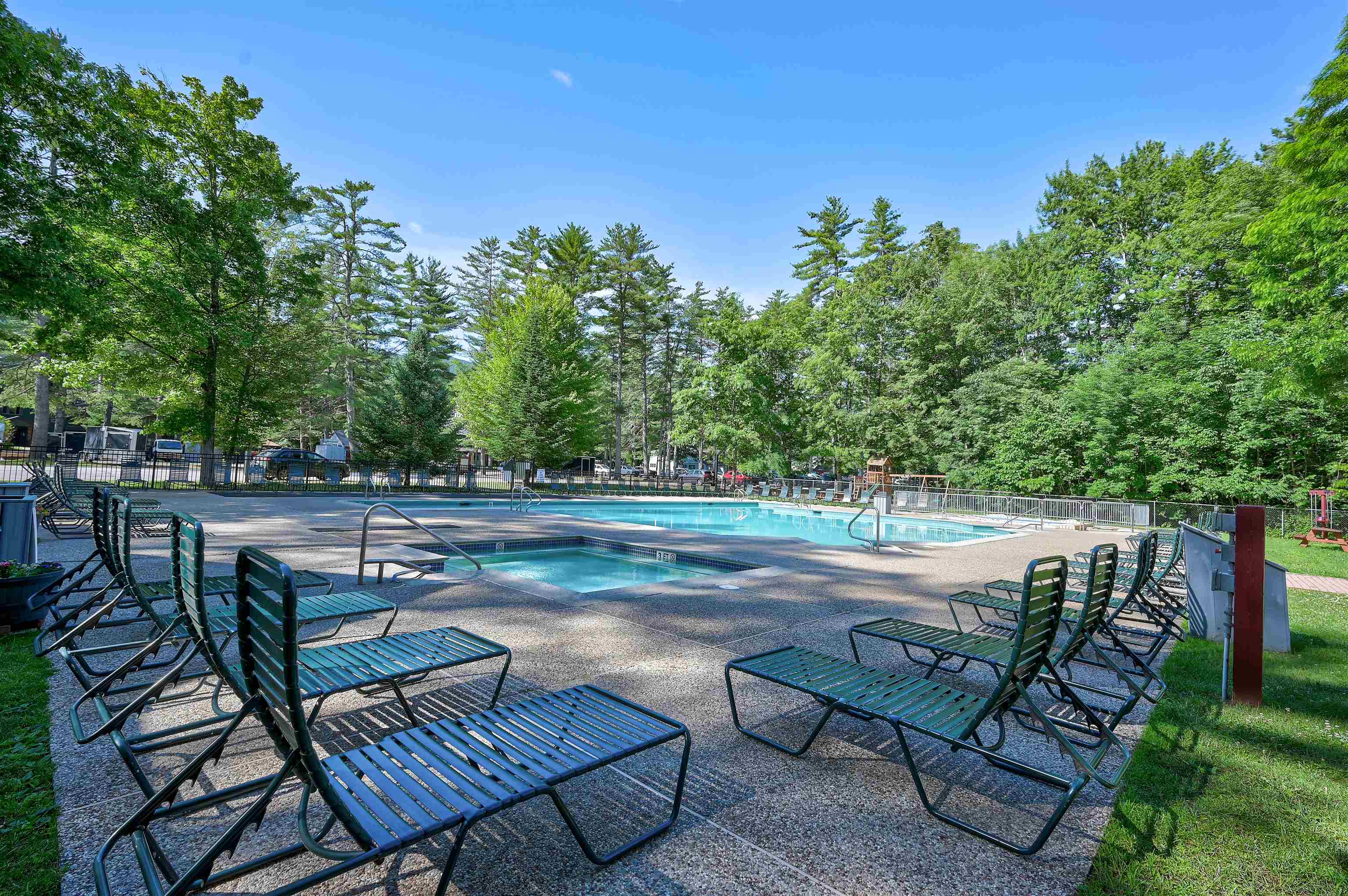 Outdoor swimming pool and wading pool with lounge chairs beneath mature trees.