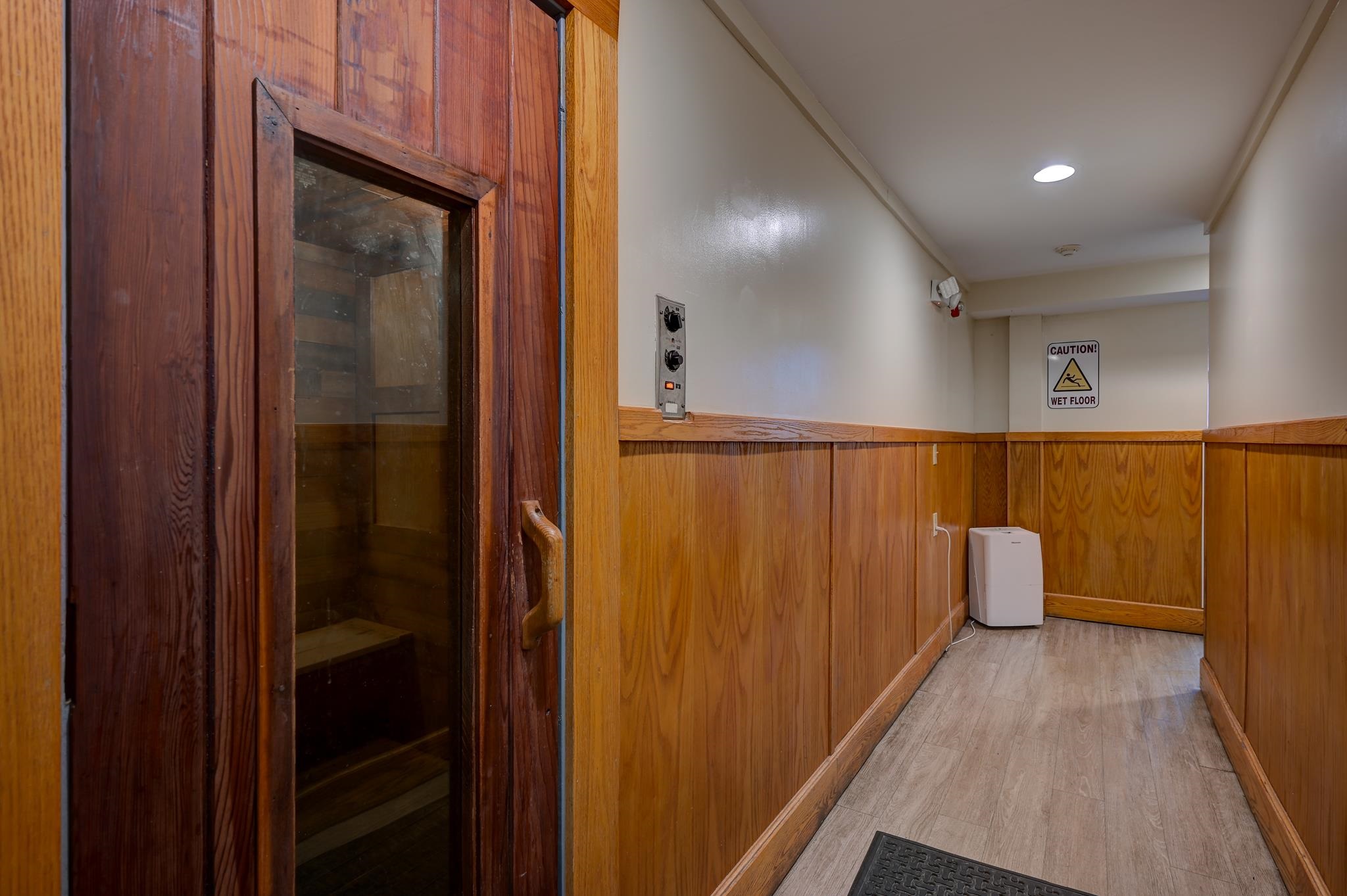 Wood-paneled hallway beside a wood-framed sauna door, with a wet-floor caution sign.