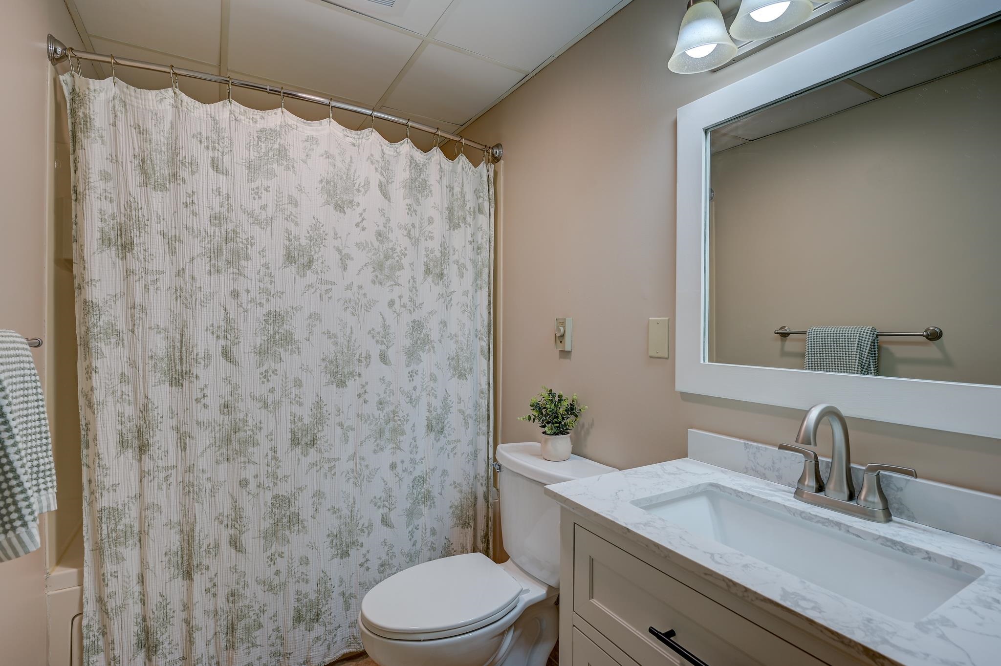 Bathroom with a floral shower curtain and marble-look vanity.