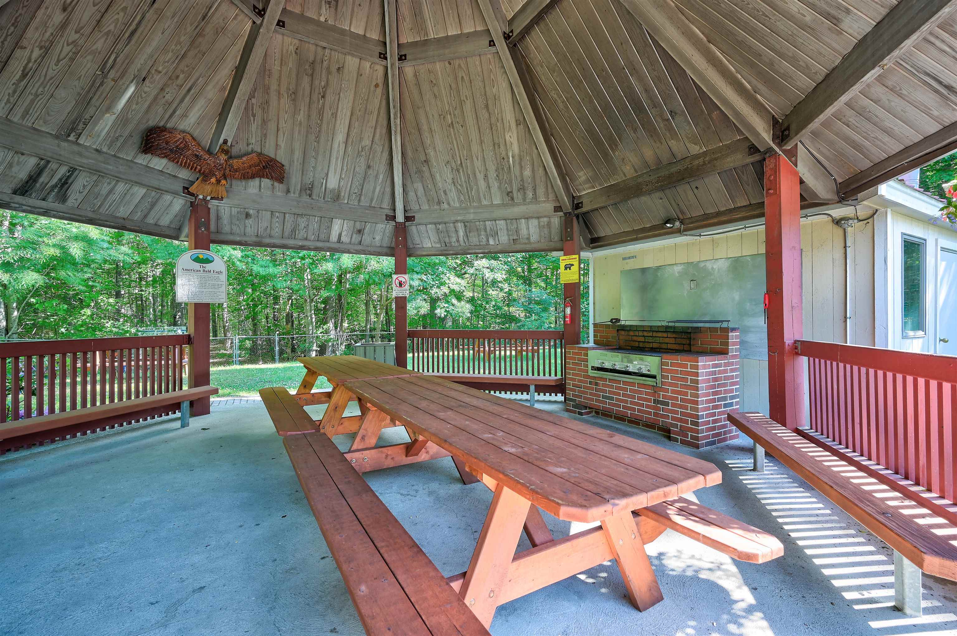 Covered picnic pavilion with a wooden table, brick grill, red railings, and carved eagle.