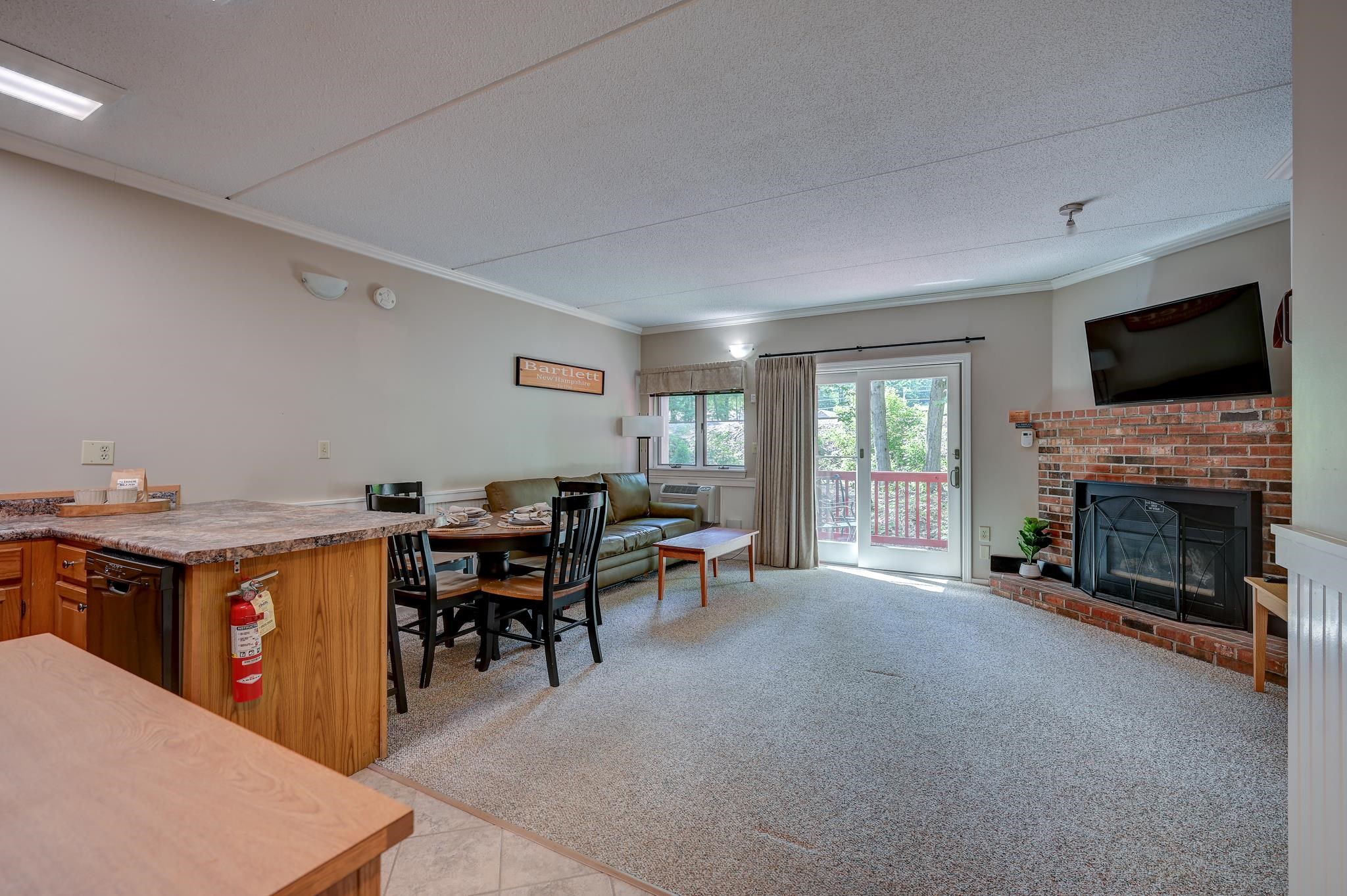 Open living and dining area with a brick fireplace, green sofa, and sliding doors to a balcony.