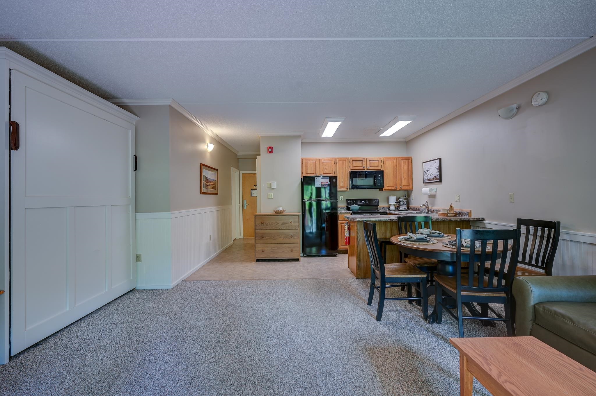 Open-plan condo kitchen and dining area with wood cabinets, a round table, and carpeted living space.