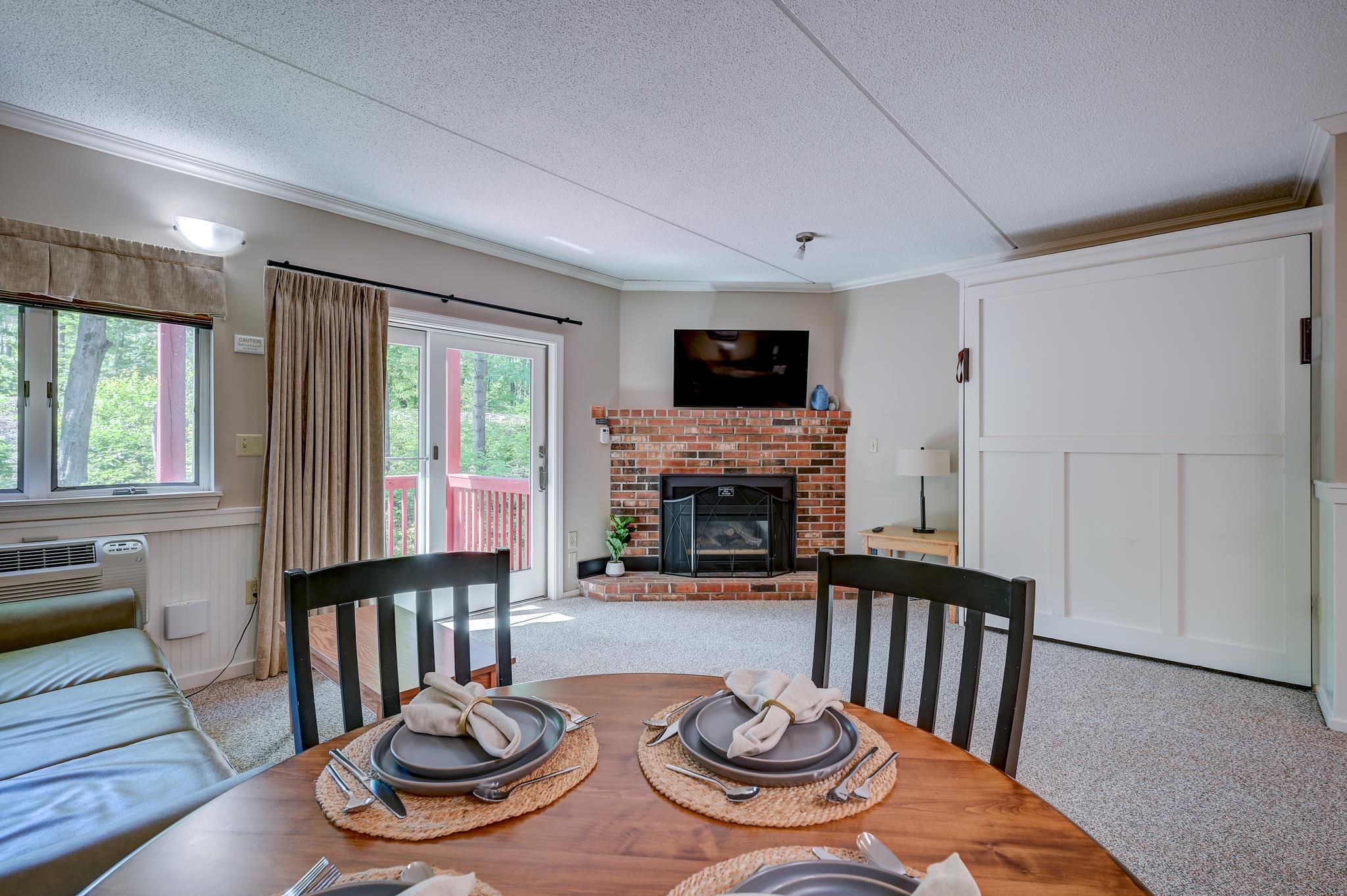 Staged living and dining area with a brick fireplace, round set table, and sliding glass doors.