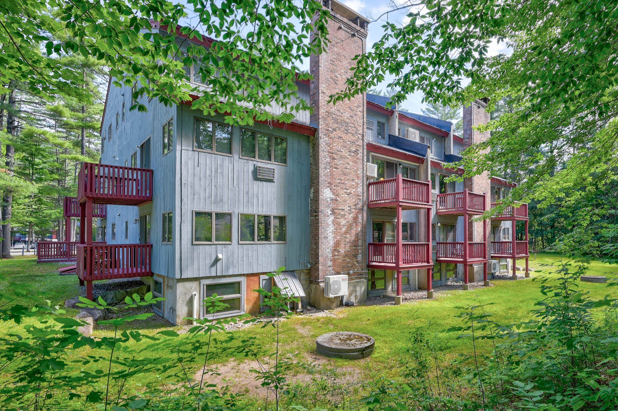 Condominium building with red balconies and brick chimneys among summer trees.