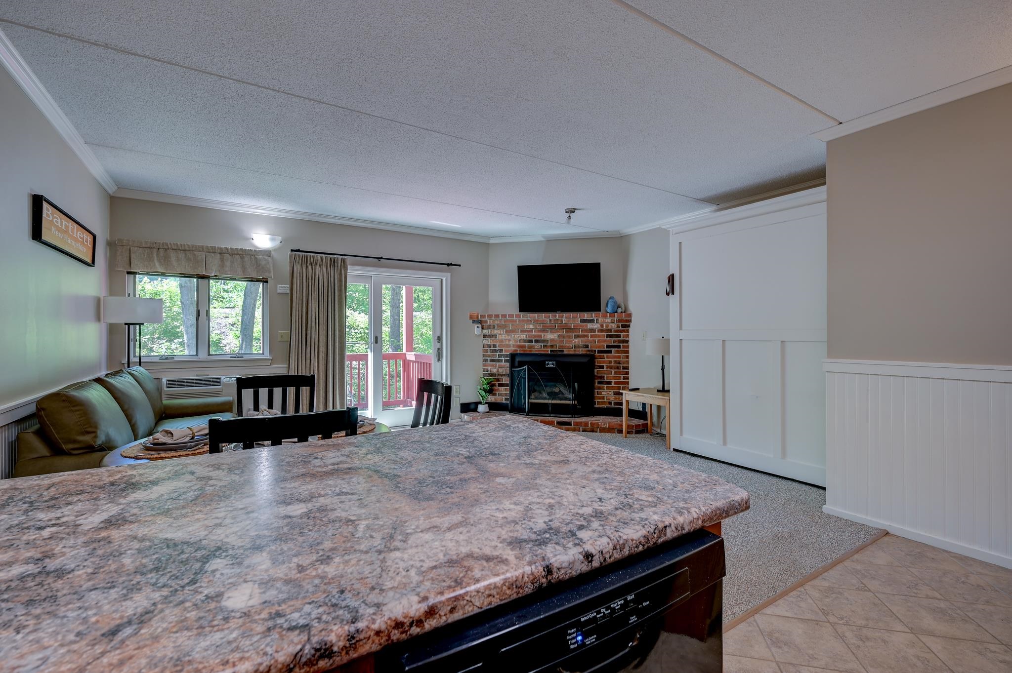 Furnished living room with a brick fireplace, large counter, and glass door to a red-railed deck.