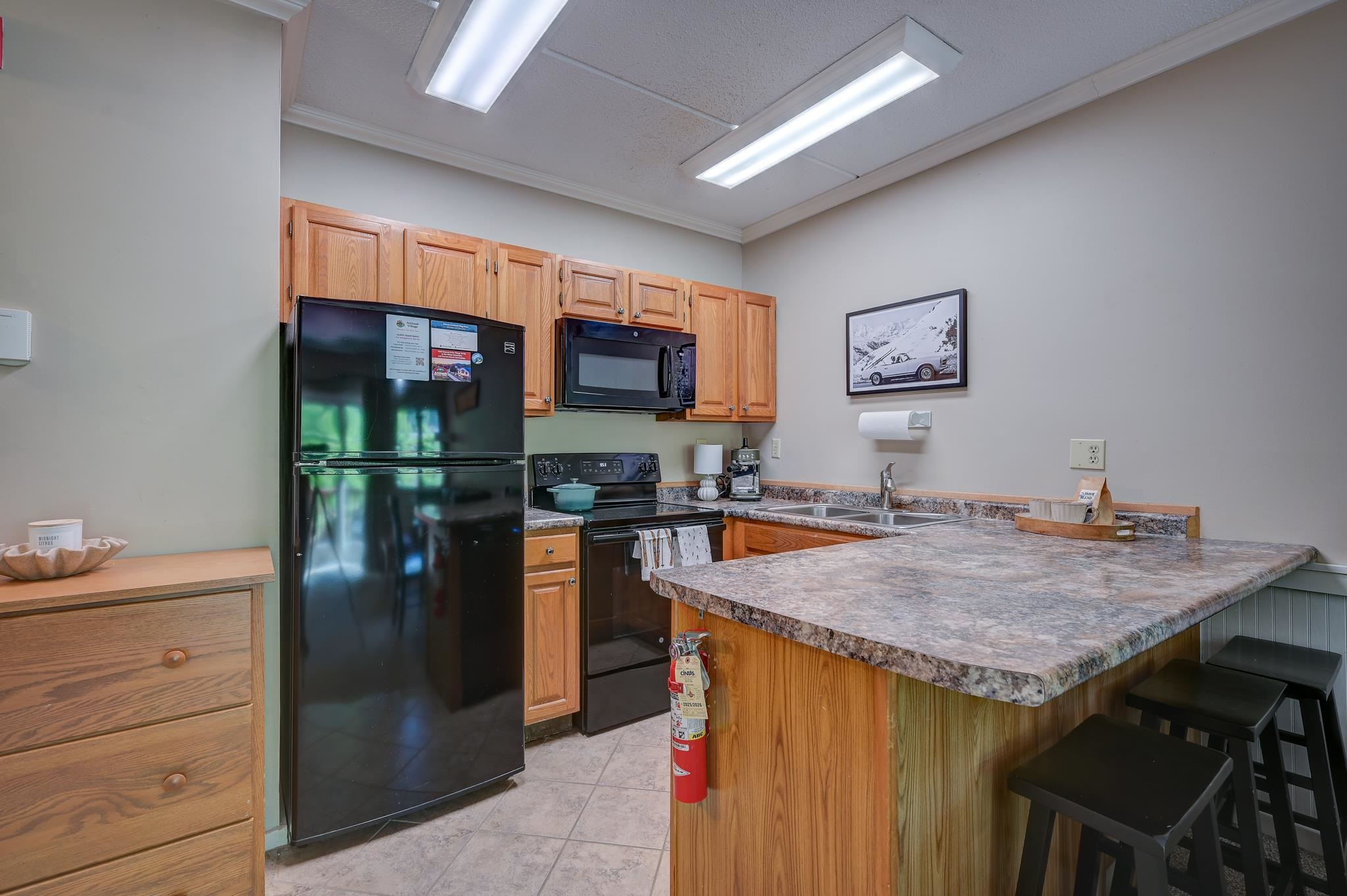Kitchen with wood cabinets, black appliances, and a large island with bar stools.