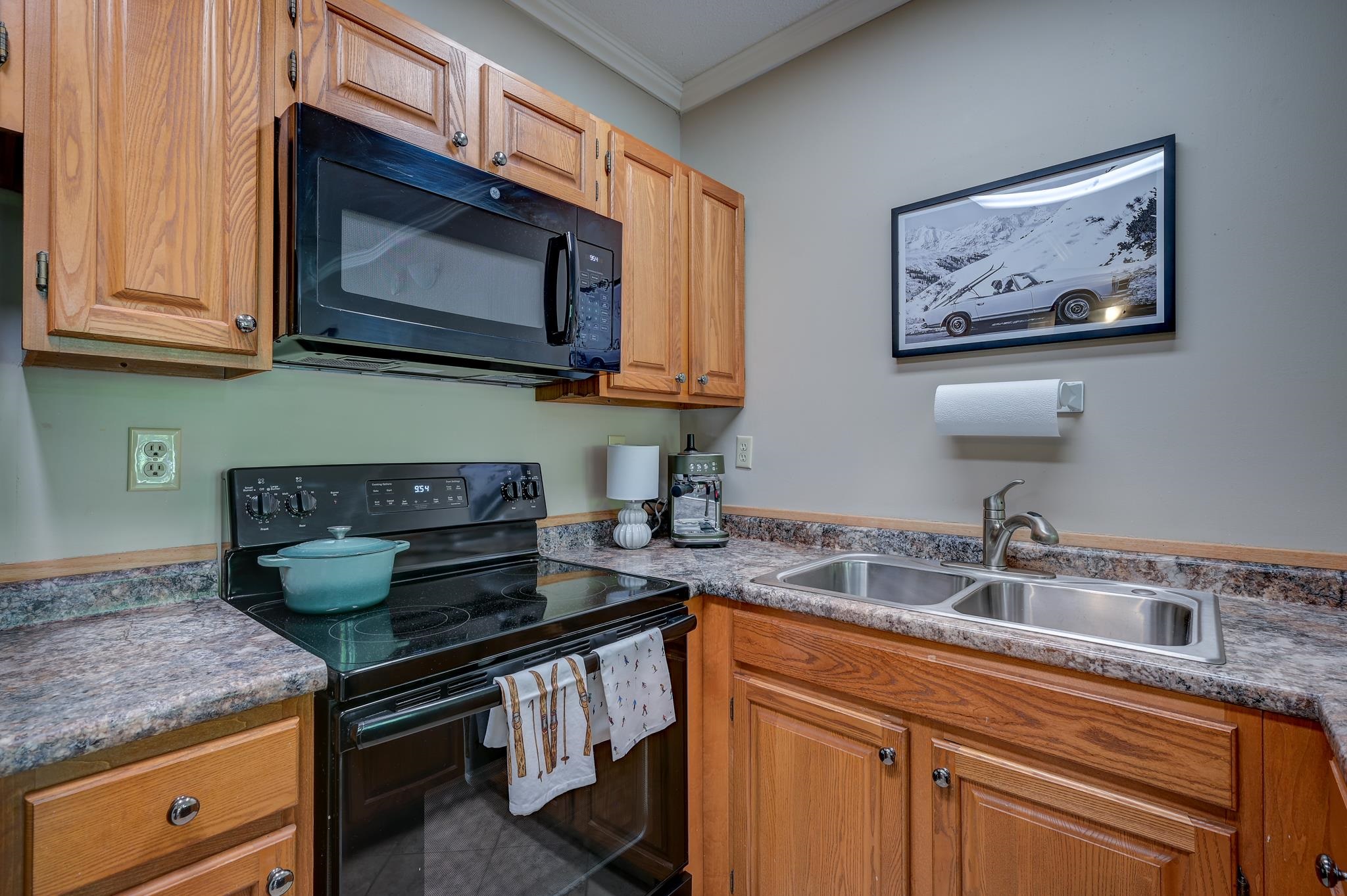 Kitchen with wood cabinets, a black range and microwave, and a double-basin stainless steel sink.