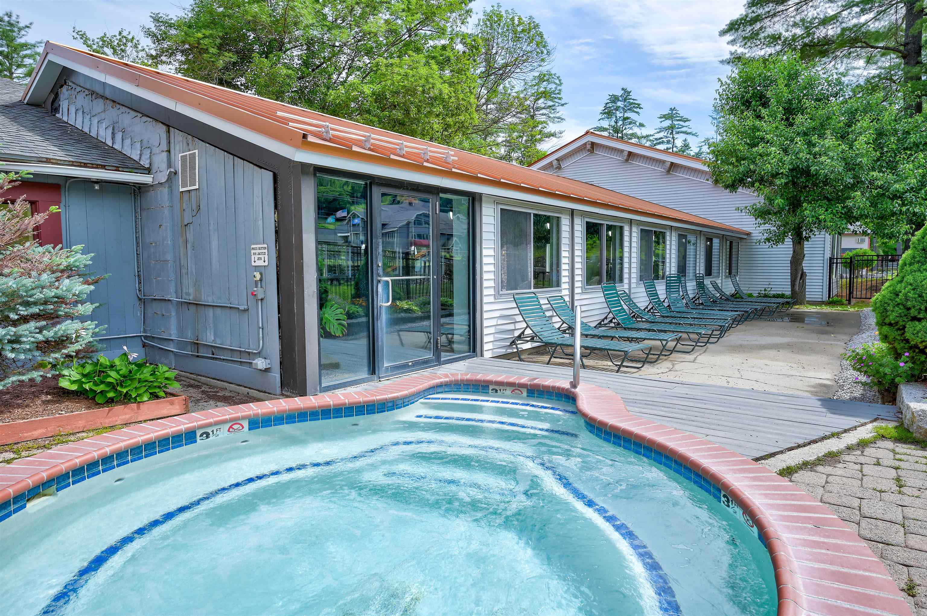 Outdoor swimming pool beside a low-rise building, with a row of lounge chairs.