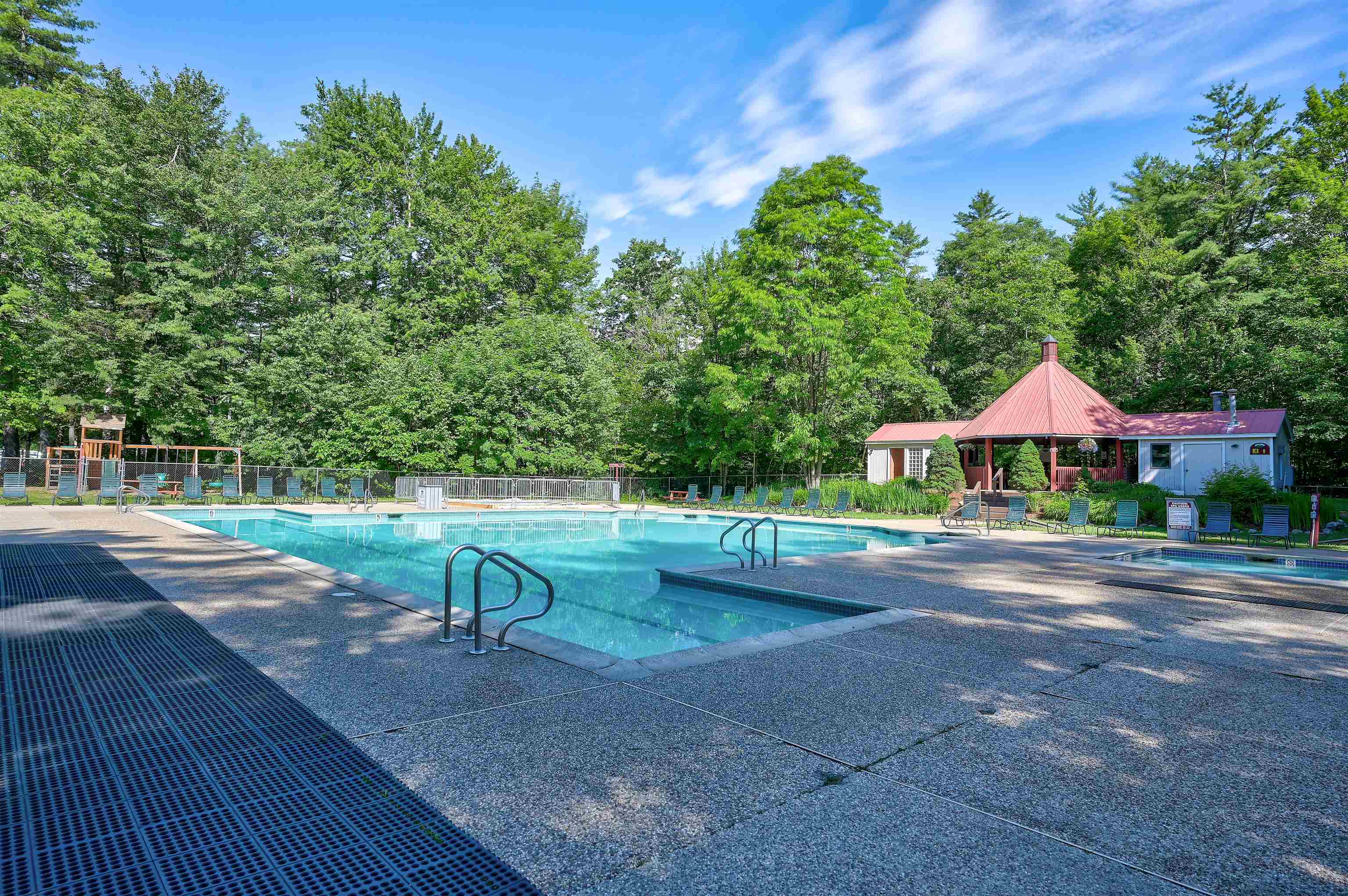 Outdoor swimming pool with lounge chairs and a red-roofed pavilion, surrounded by trees.