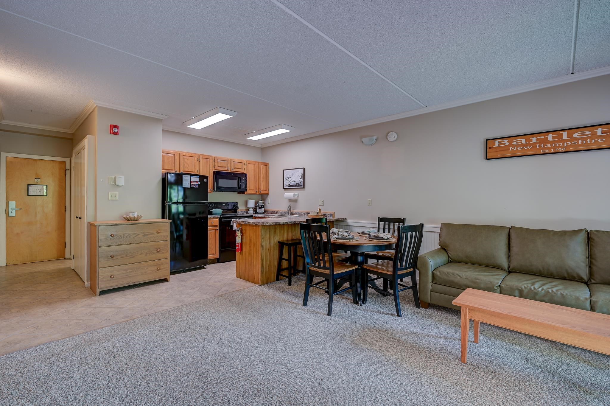 Open-plan living area with a wood-cabinet kitchen, set dining table, and green sofa.