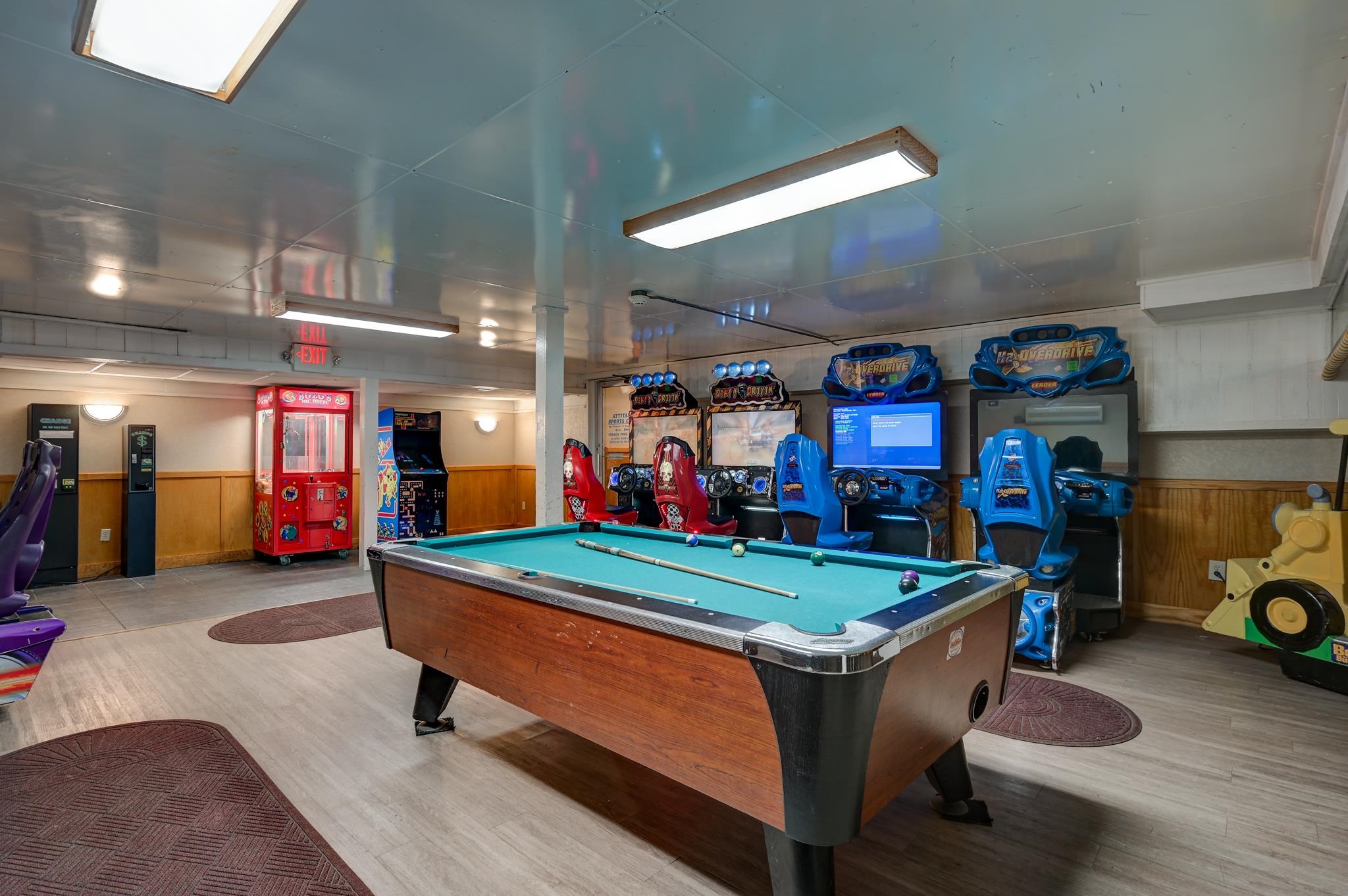 Recreation room with a pool table, arcade racing games, and a red claw machine.