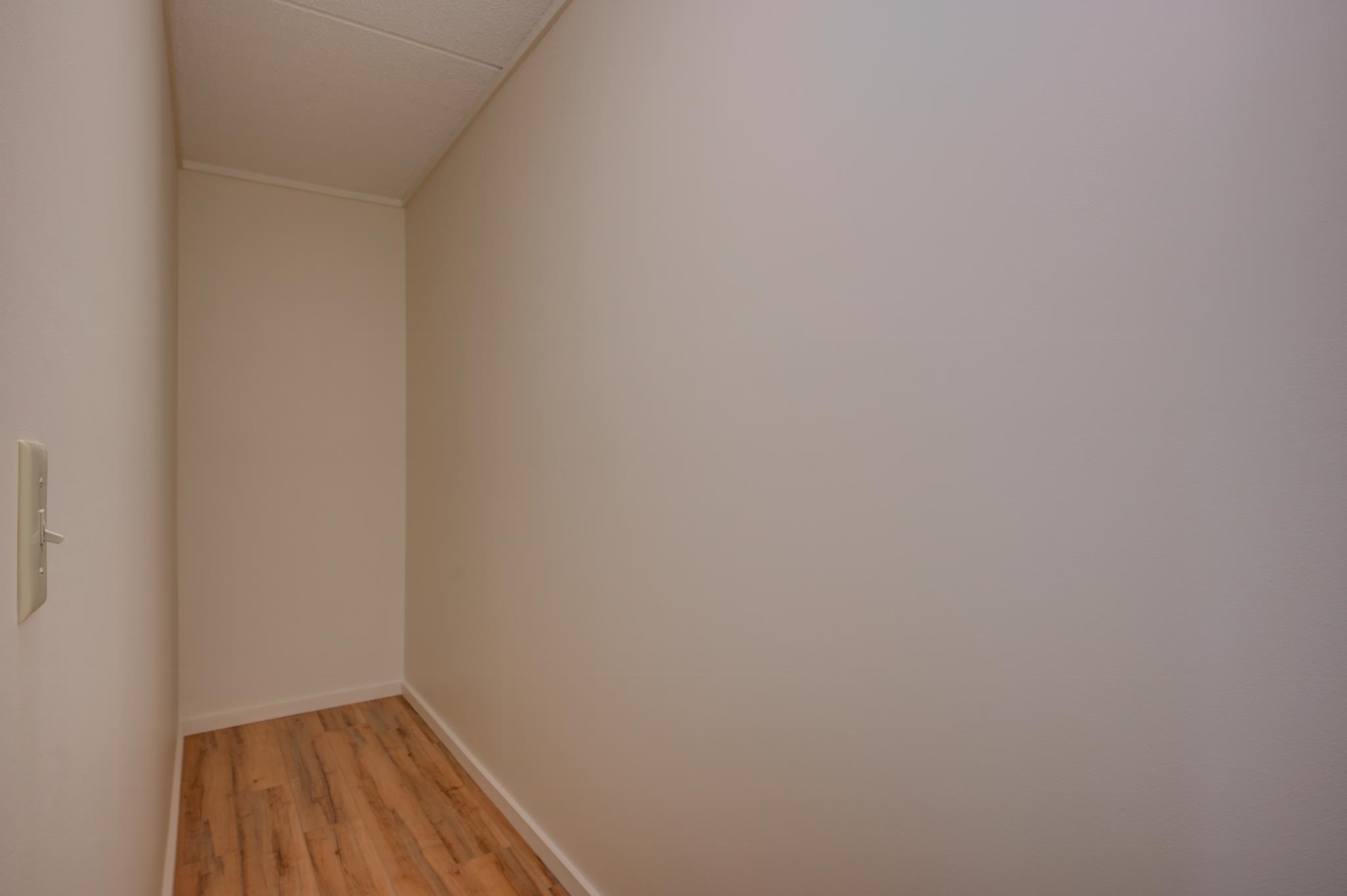 Empty narrow hallway with beige walls and warm wood-look flooring.