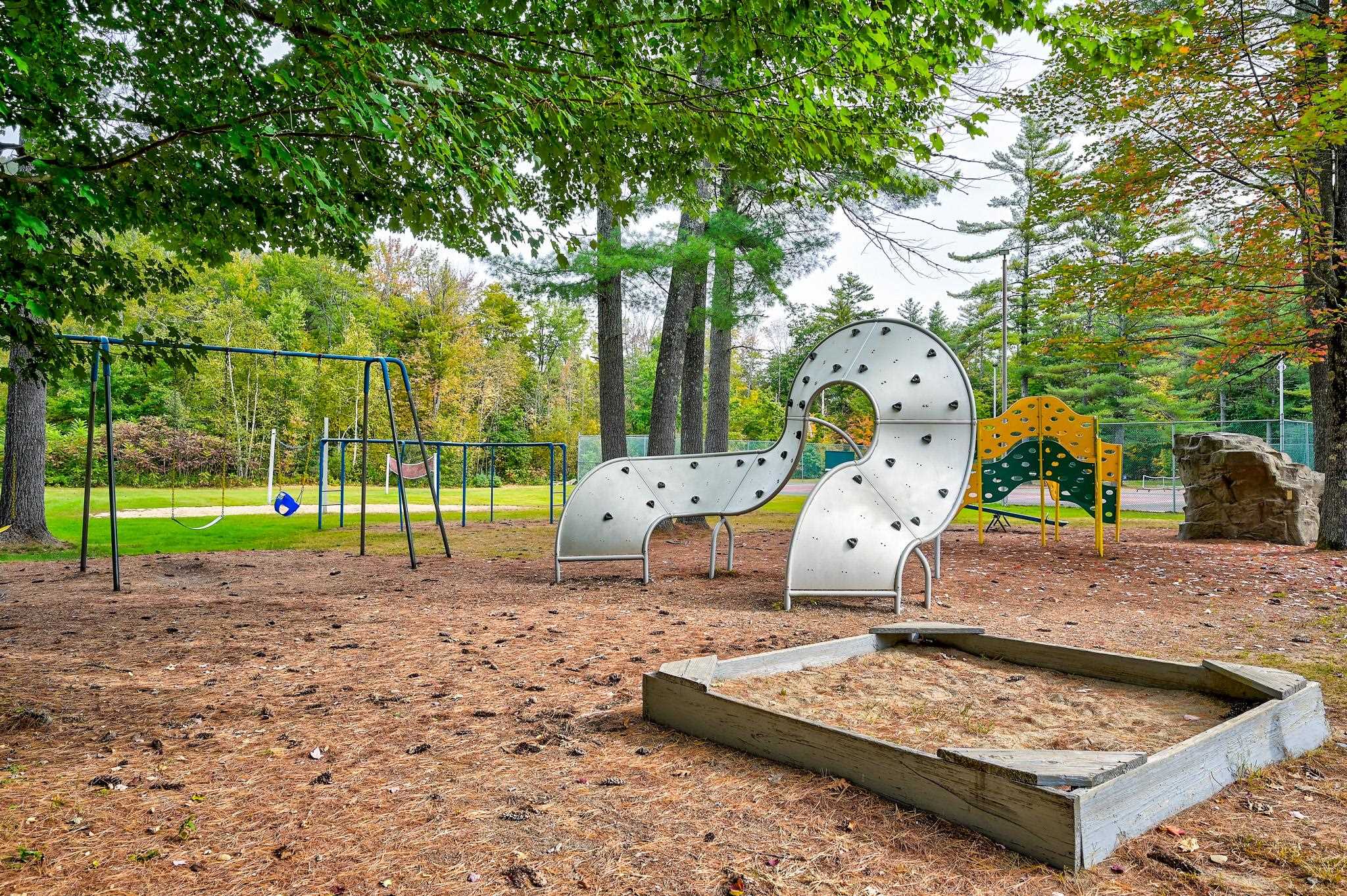 Wooded playground with climbing structure, swings, and a sandpit.