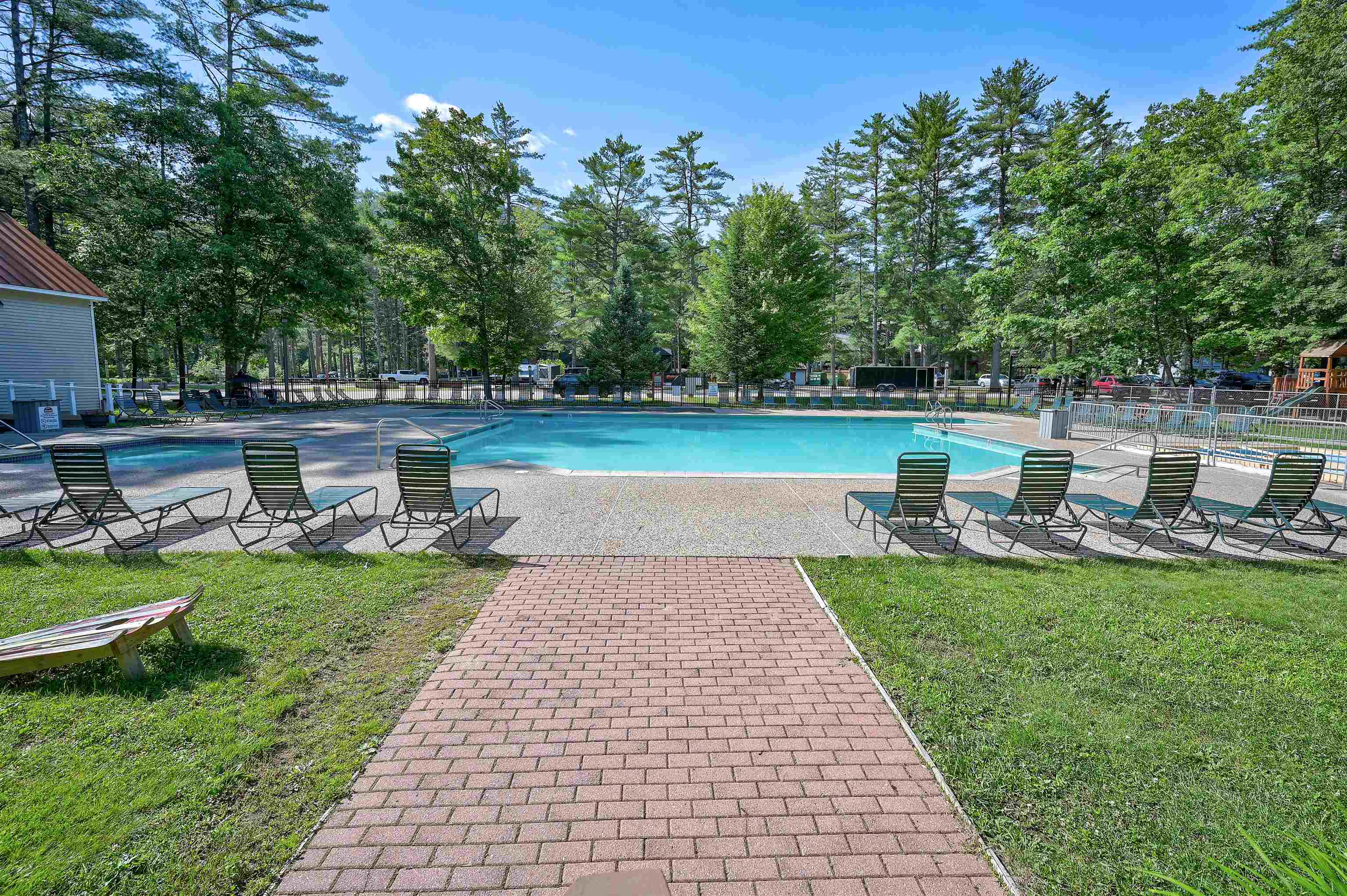 Outdoor pool with lounge chairs, wooded surroundings, and a brick walkway.