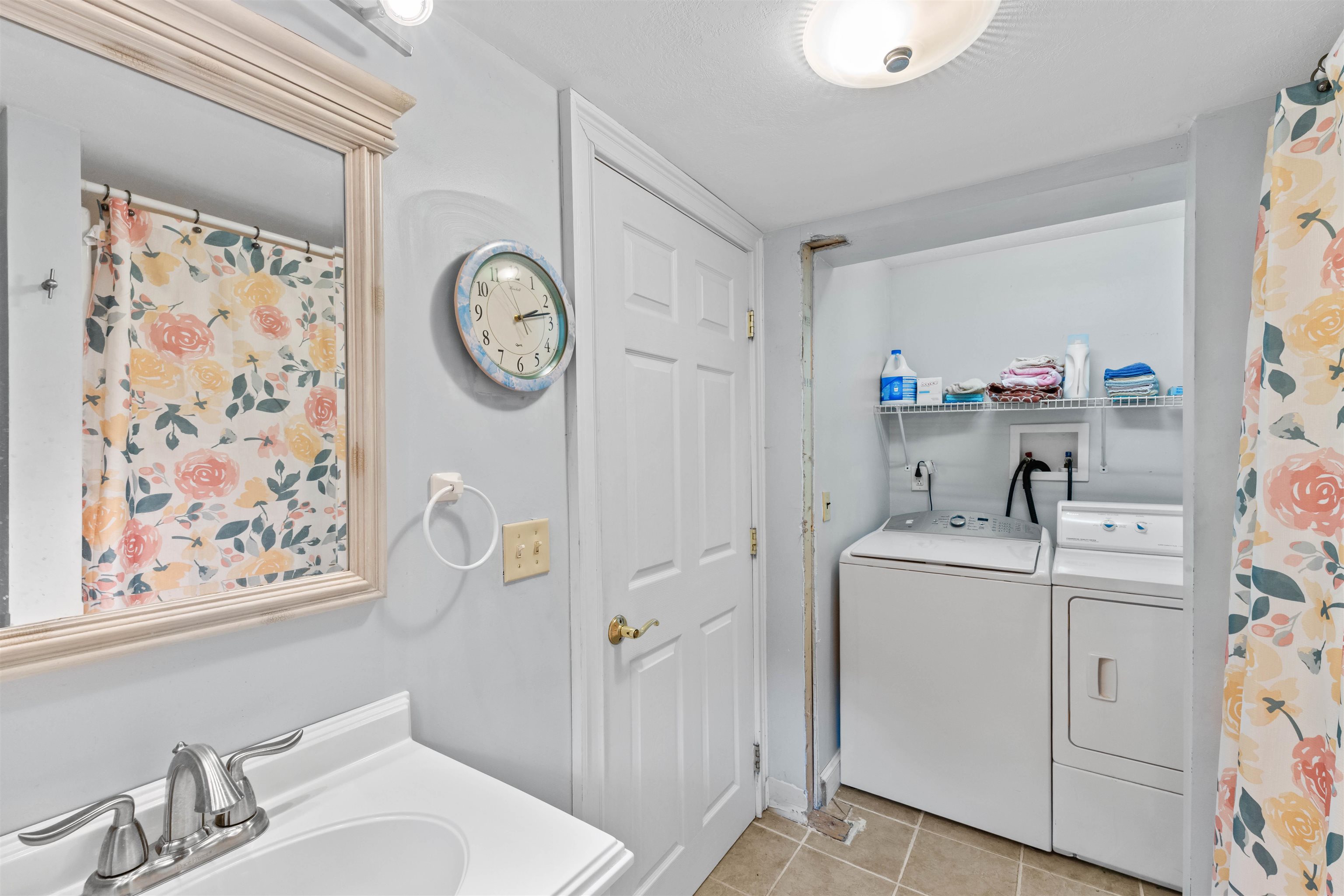 Laundry room with washer and dryer, towel shelf, and floral curtains beside a vanity sink.