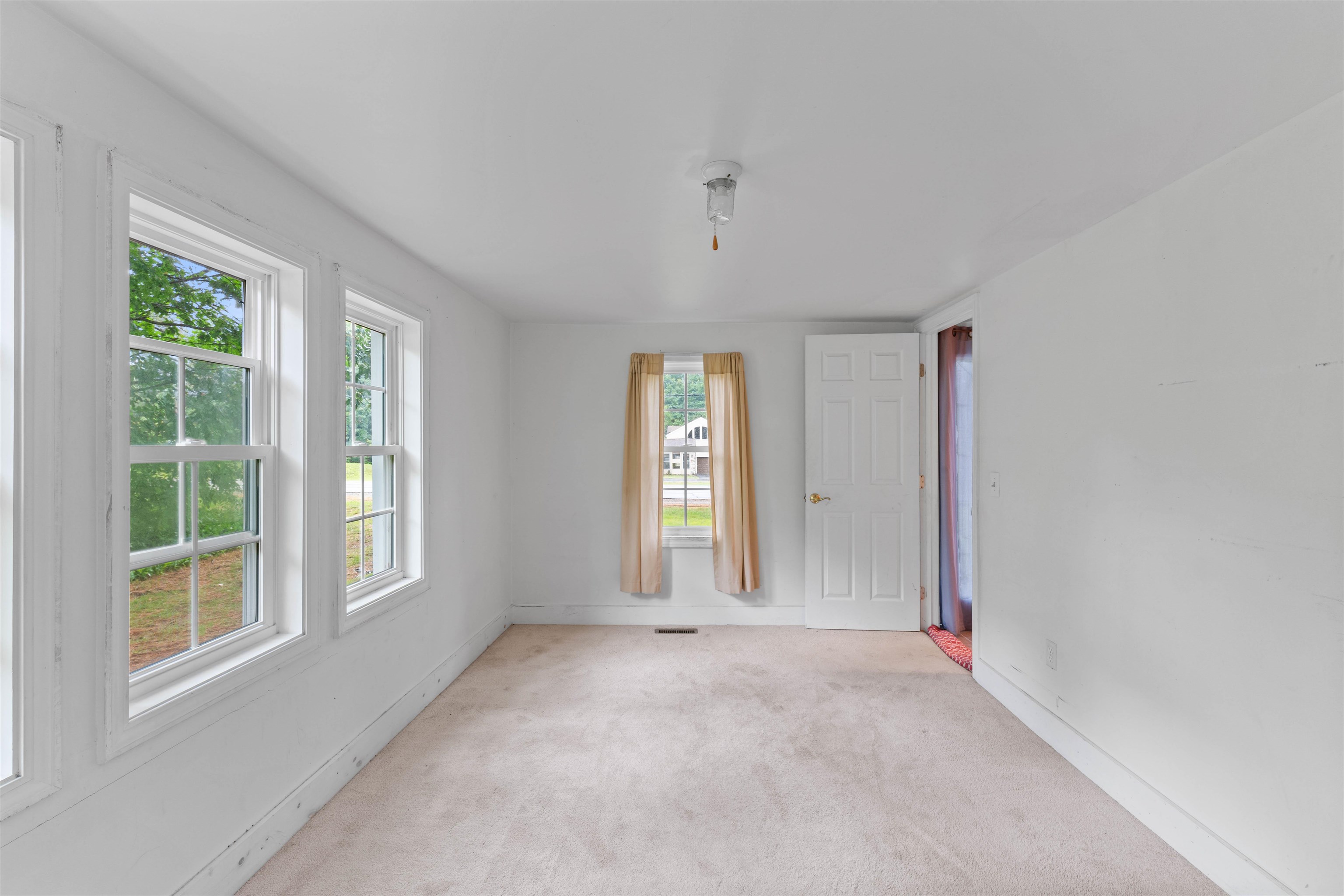 Empty carpeted room with large windows and a small curtained window.