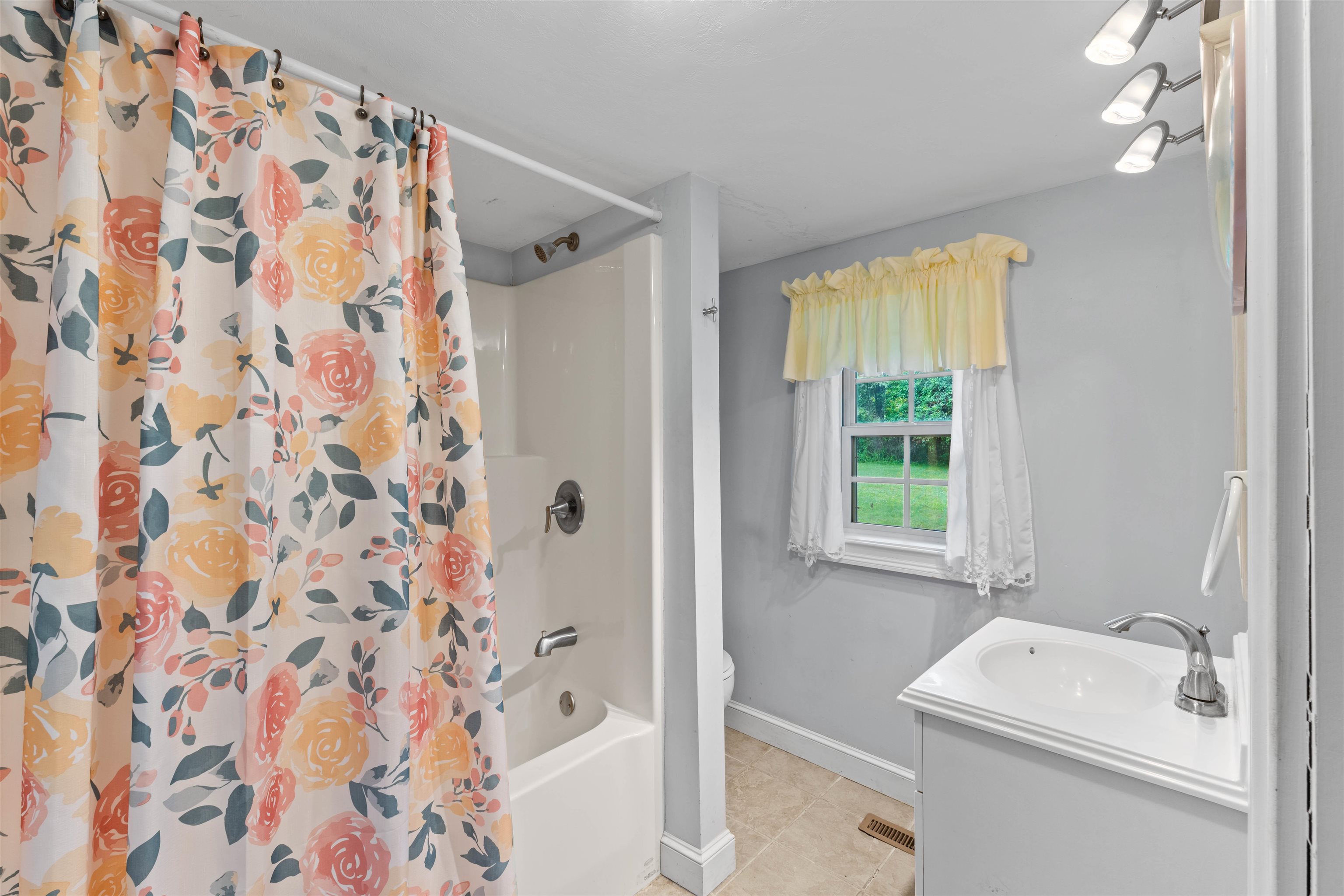 Bathroom with a floral shower curtain, white vanity, and curtained window.