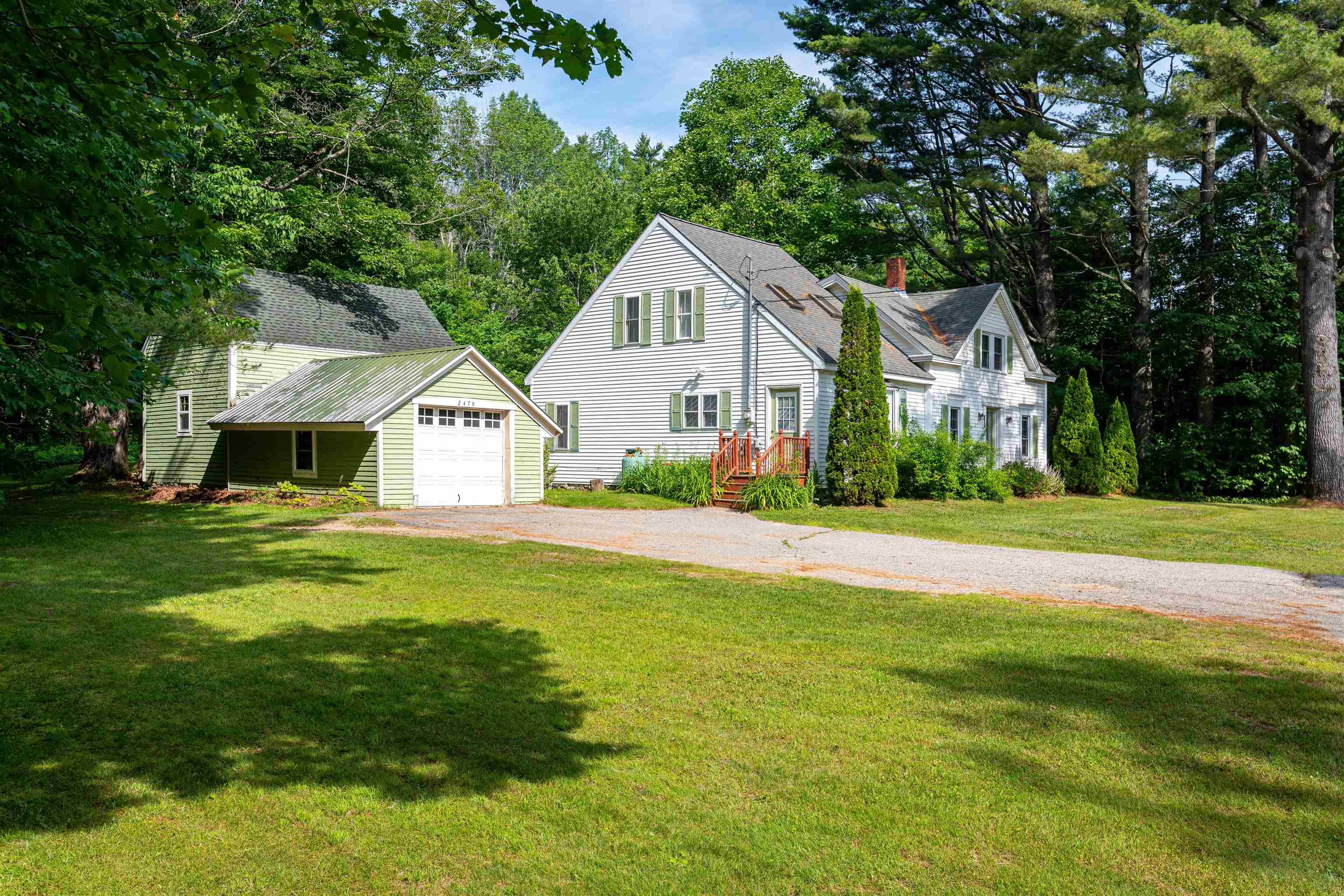 White-sided home with a pale green garage, red entry steps, and a tree-lined lawn.