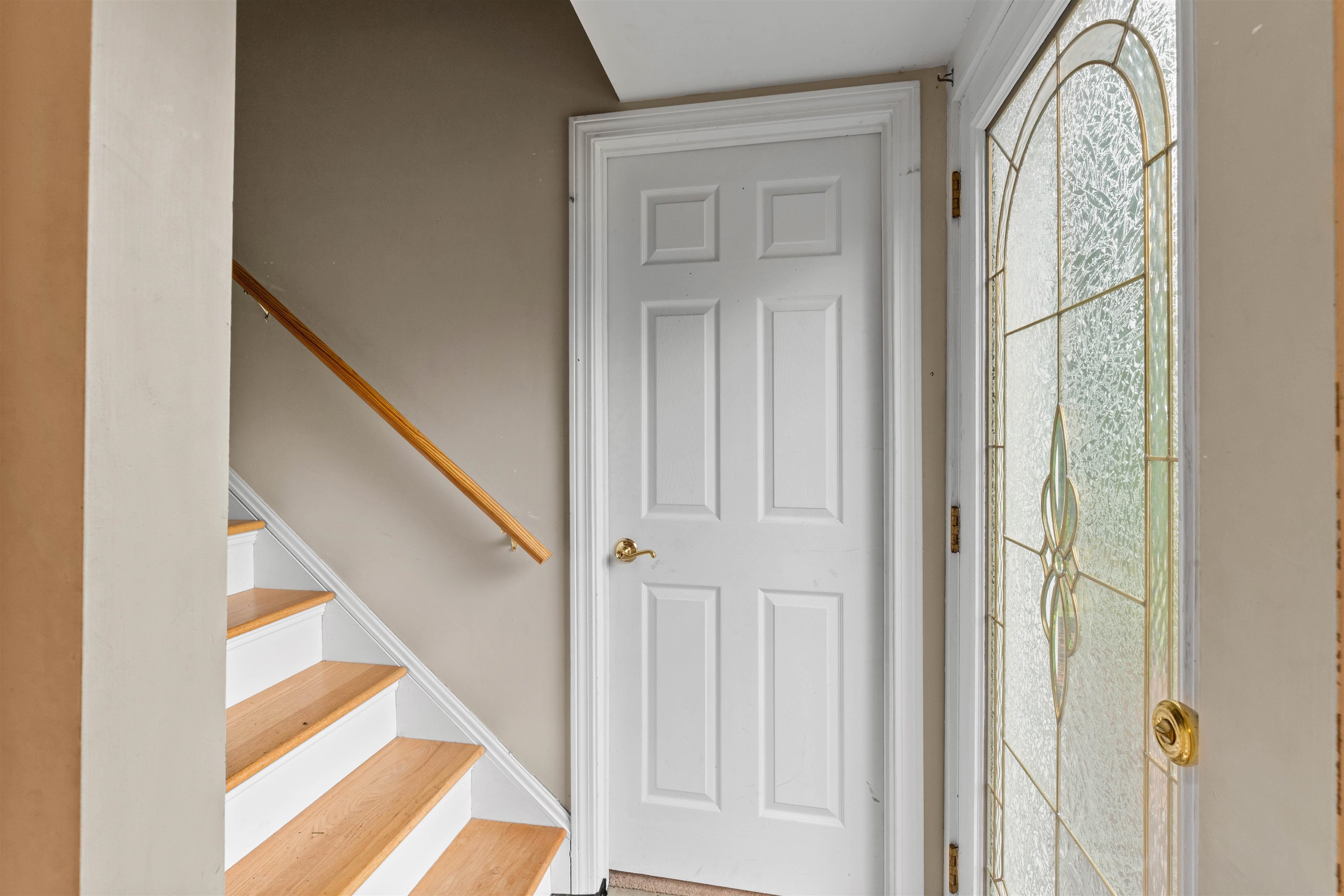 Entryway with a paneled front door, decorative glass sidelight, and staircase with light wood treads.