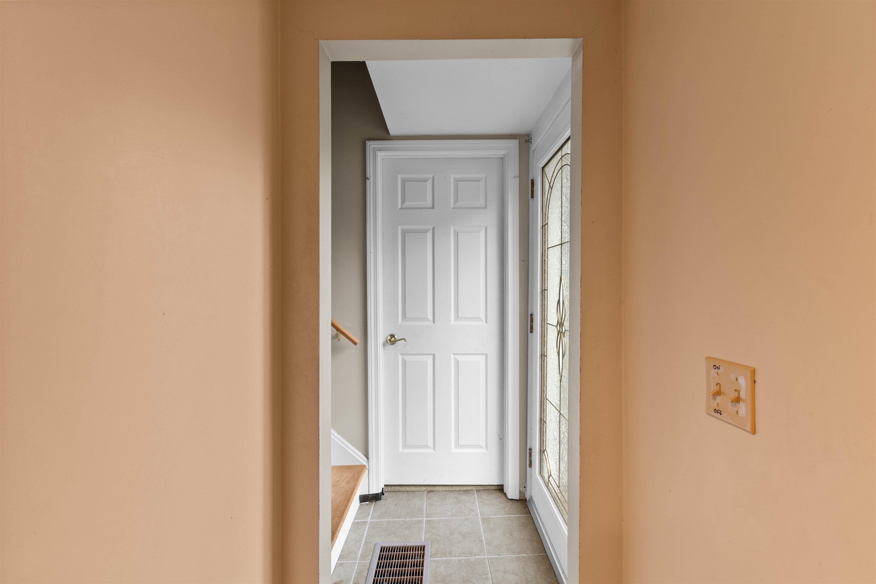 Entryway with a white paneled door, decorative glass sidelight, and tiled floor.
