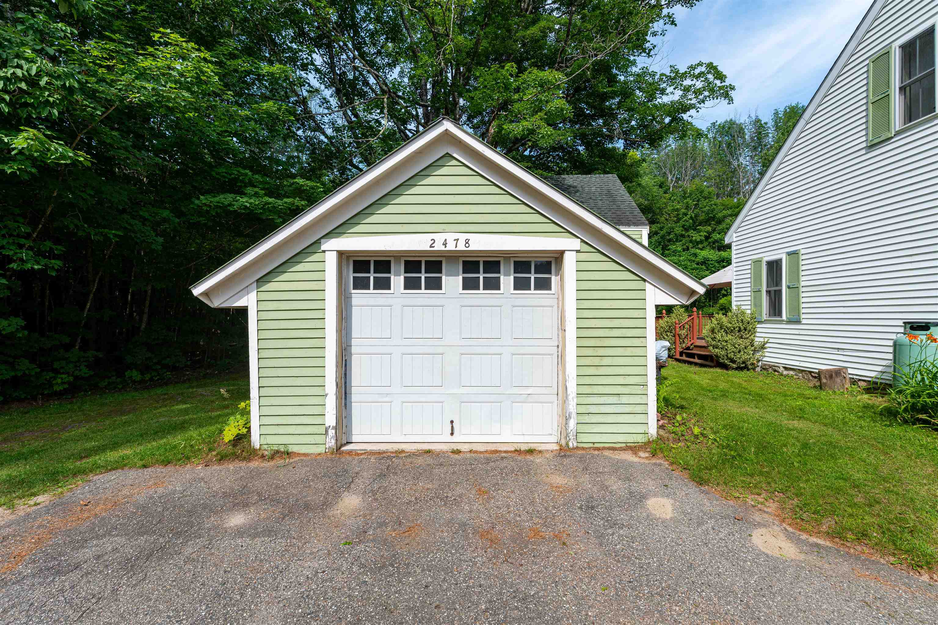 Pale green detached garage with white paneled door and 2478 above it, beside a white house.