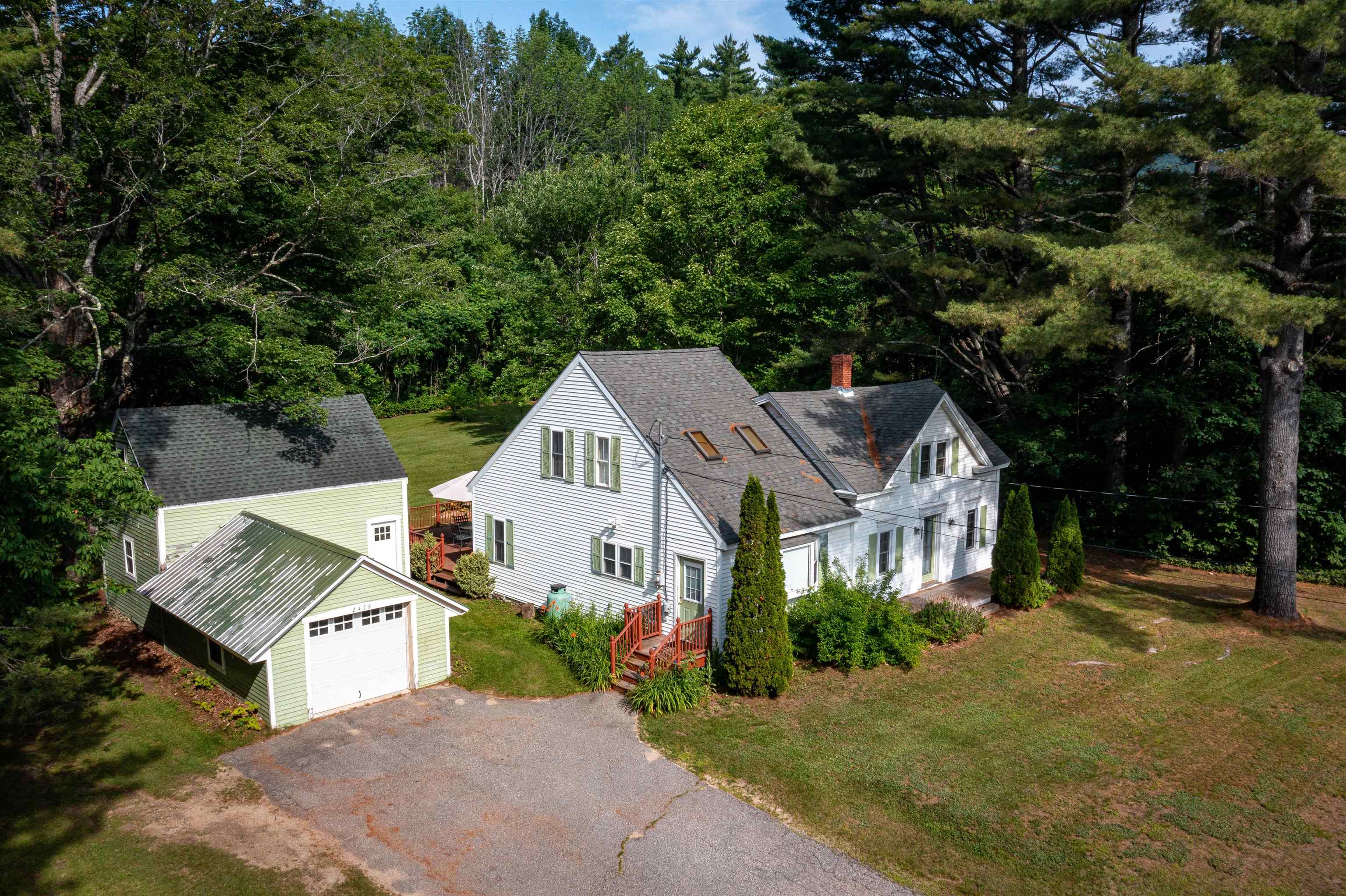 Aerial view of a white two-story house and separate pale-green garage among mature trees.