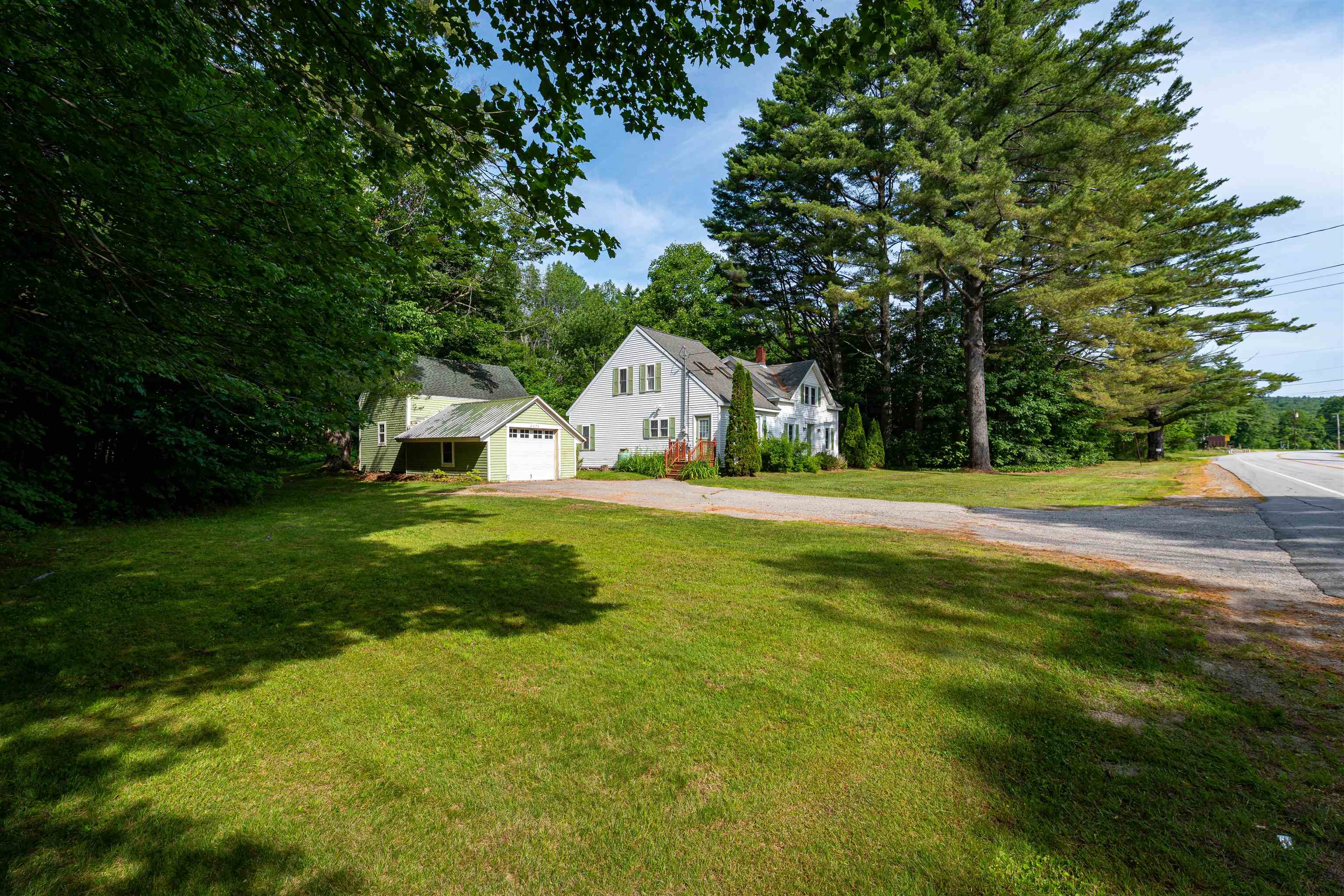 White house with an attached pale green garage, broad lawn, and gravel driveway beside the road.