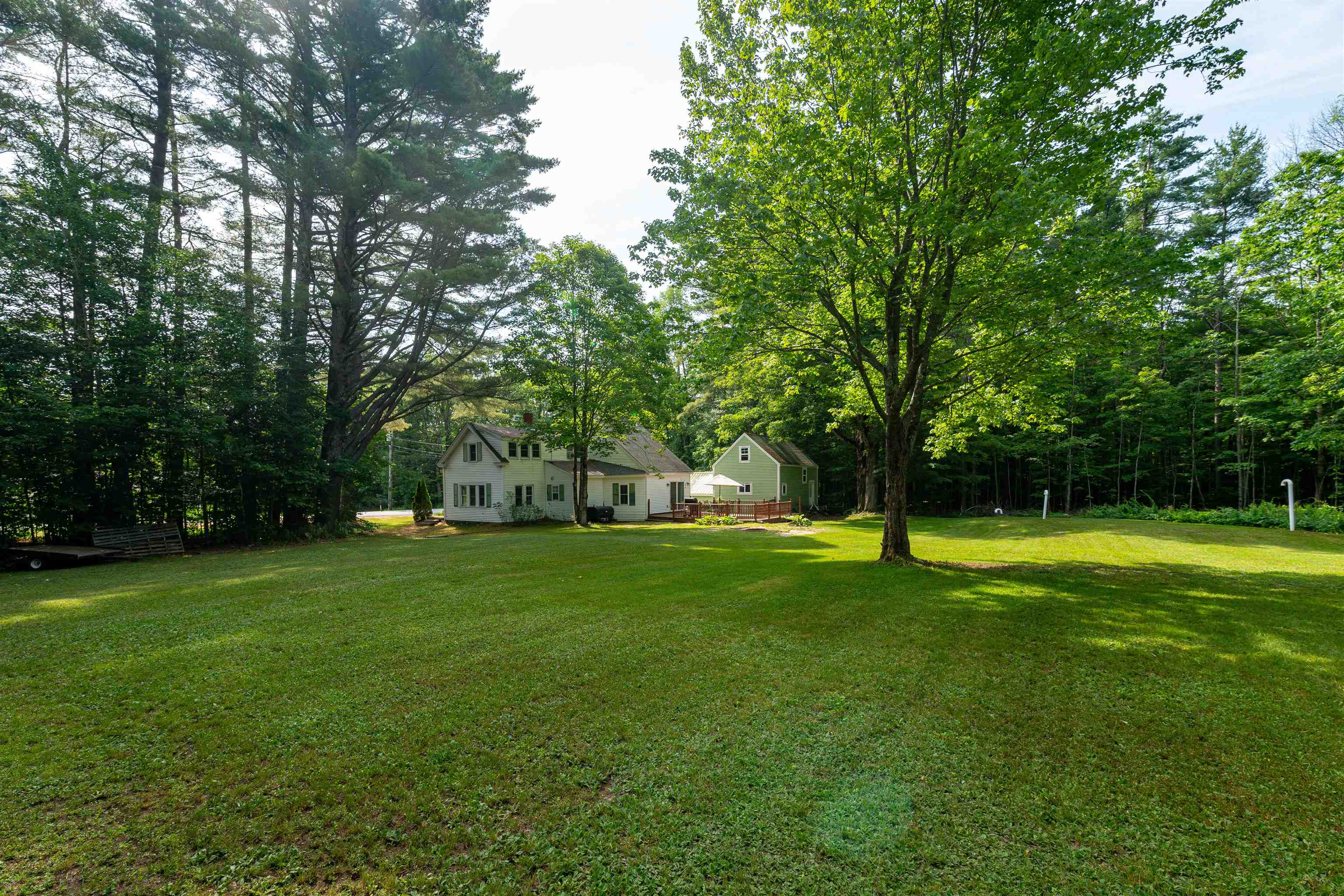House and detached outbuilding beyond a broad lawn, shaded by mature trees and bordered by woodland.