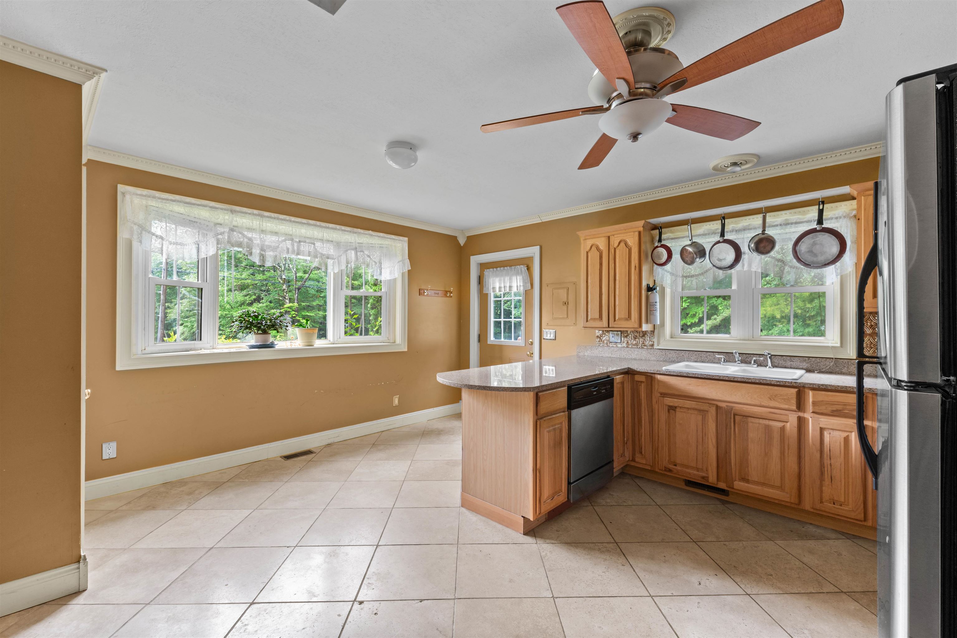 Kitchen with wood cabinets, a tiled floor, a peninsula, and large windows overlooking trees.