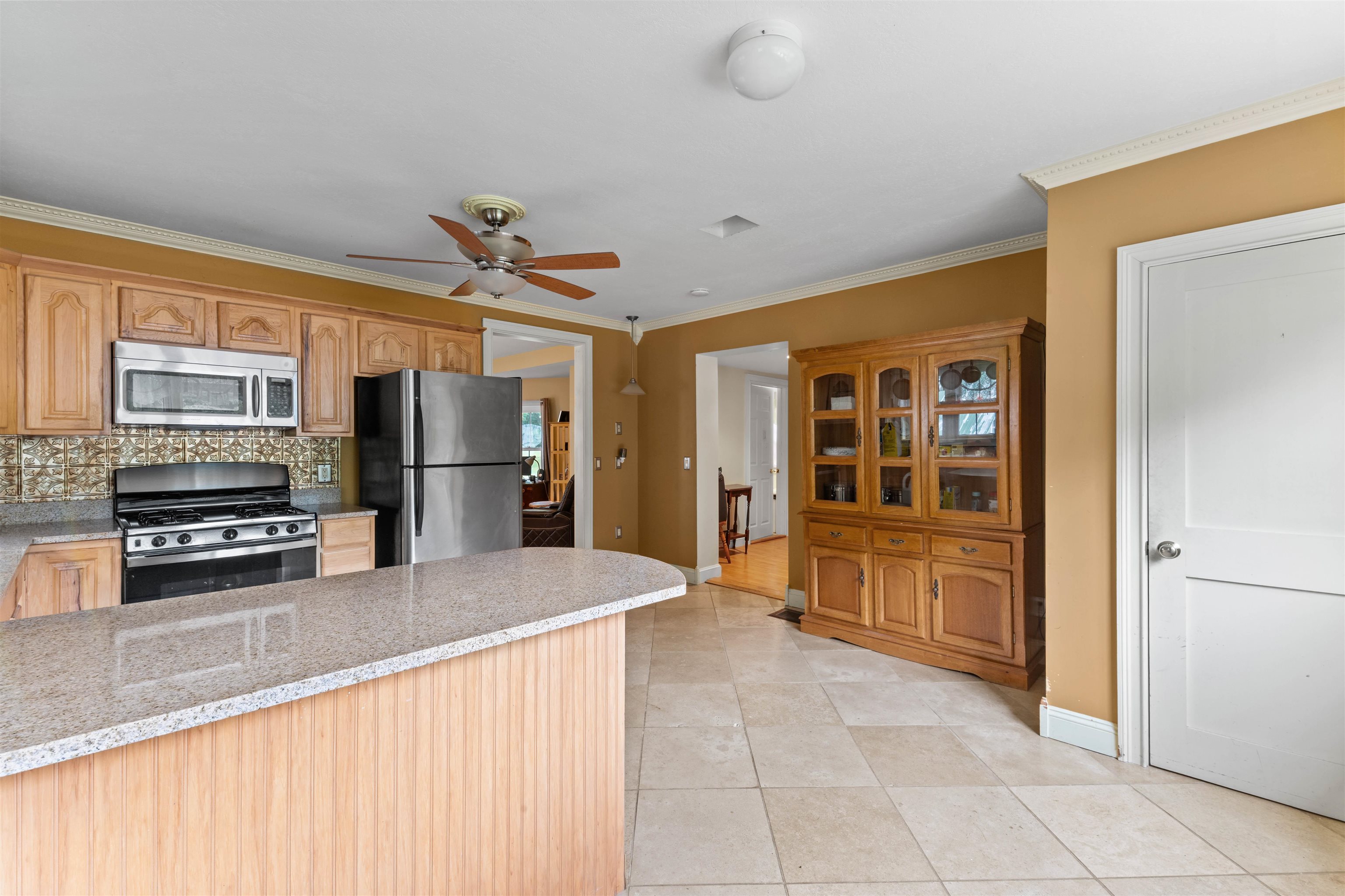 Kitchen with a large granite island, stainless steel appliances, and a glass-front wooden hutch.