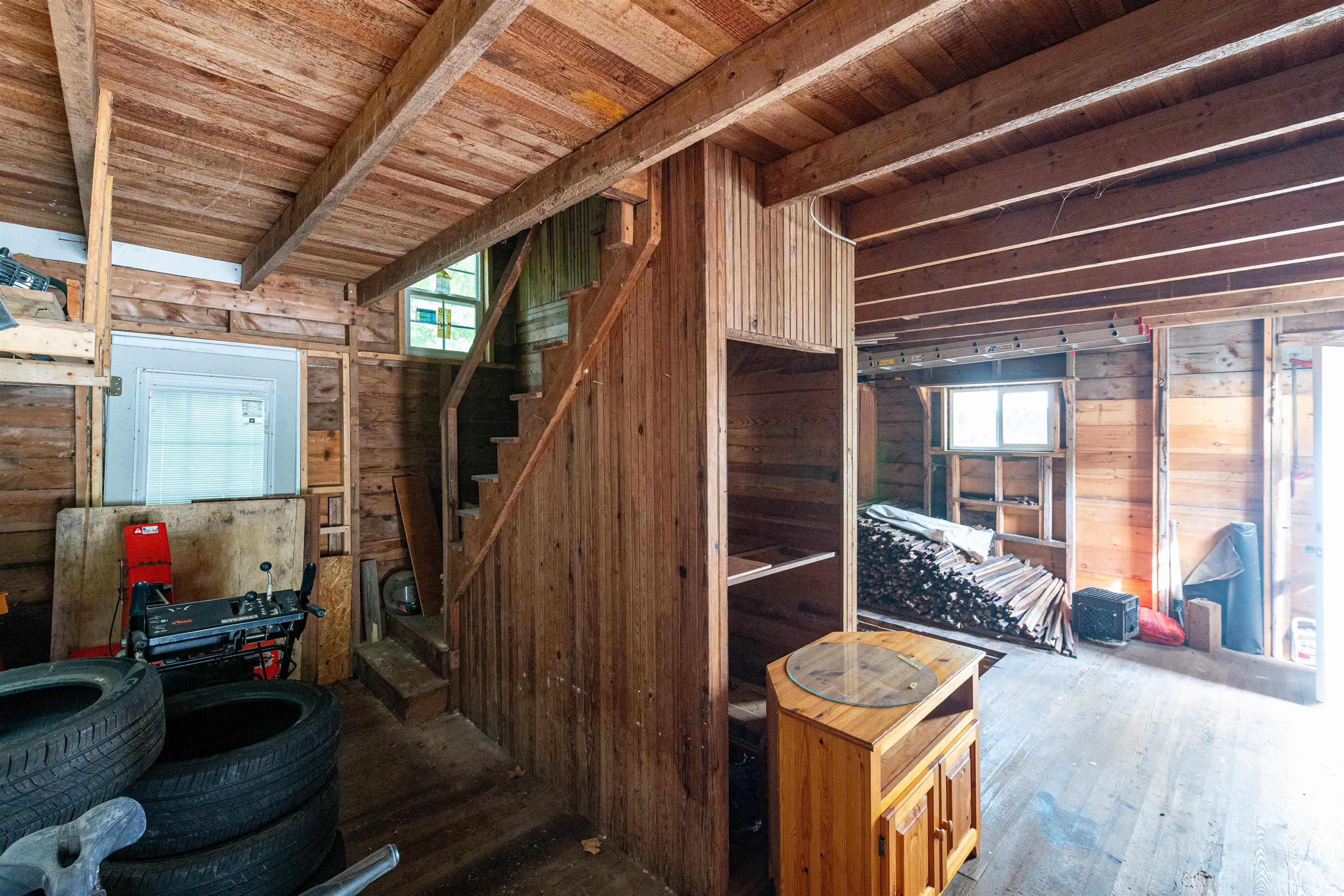 Rustic wooden garage interior with exposed beams, staircase, stacked lumber, and tires.