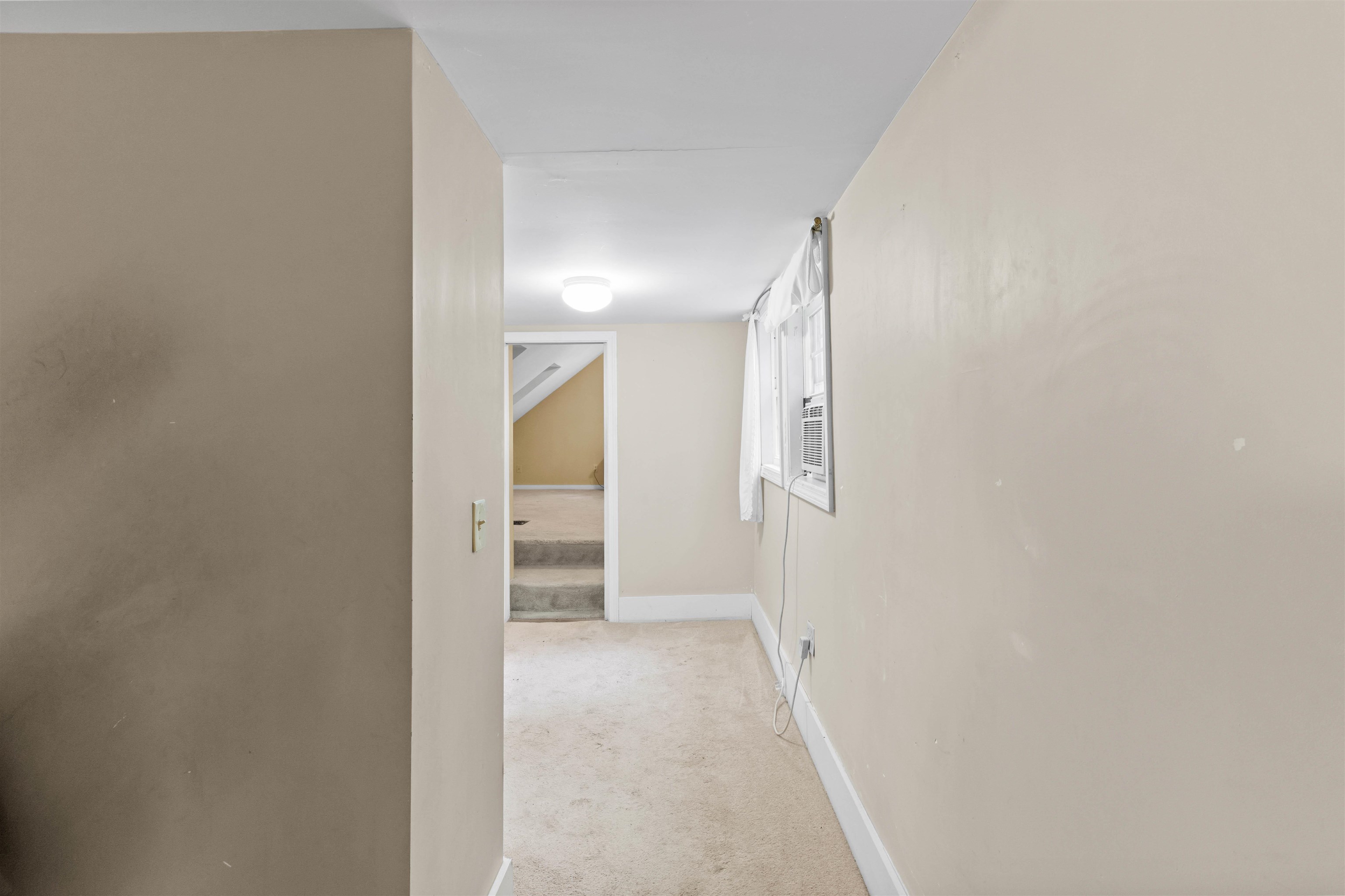 Empty carpeted room with a window air conditioner and doorway to another room.