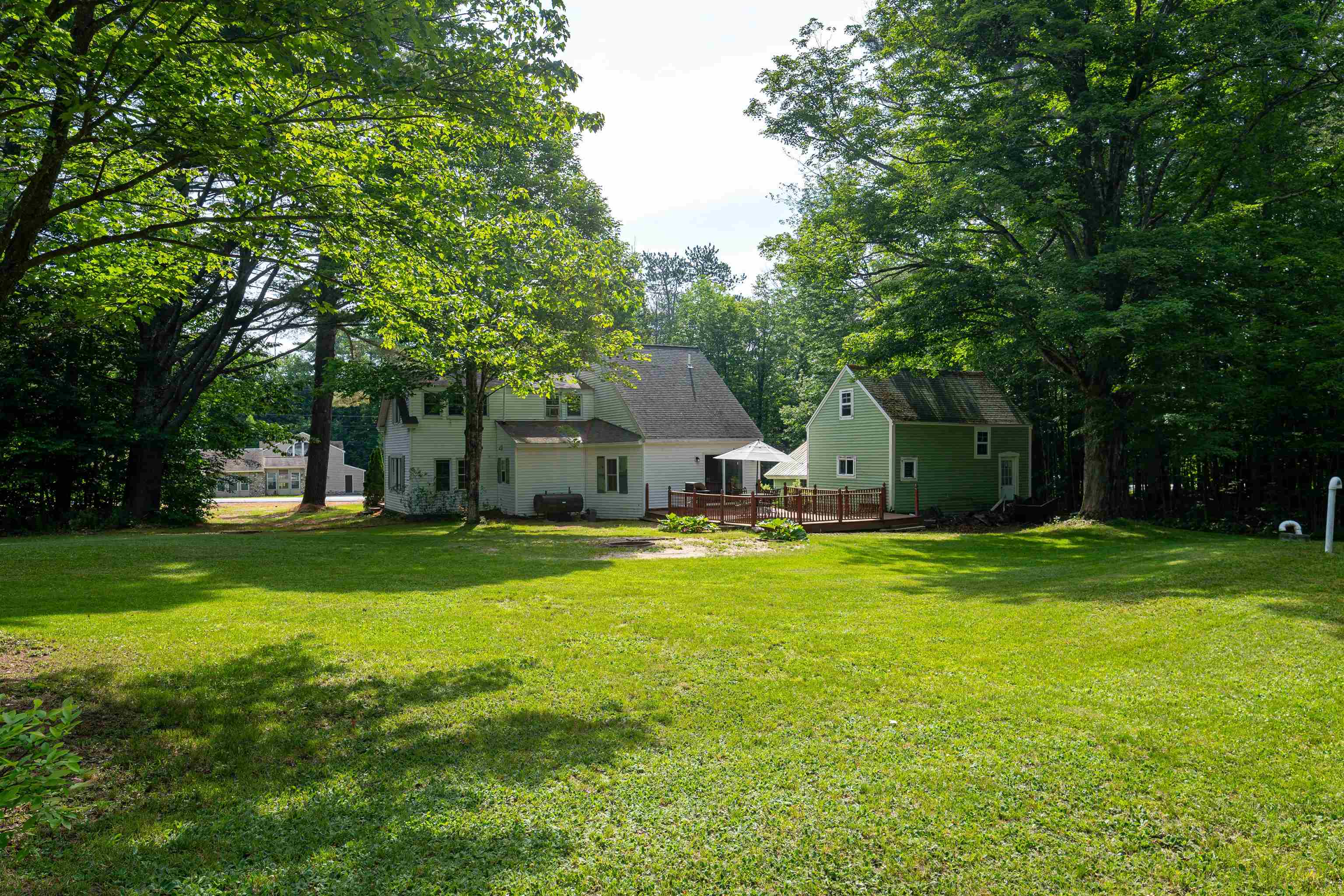 House and green outbuilding beside a deck, surrounded by trees and a broad lawn.