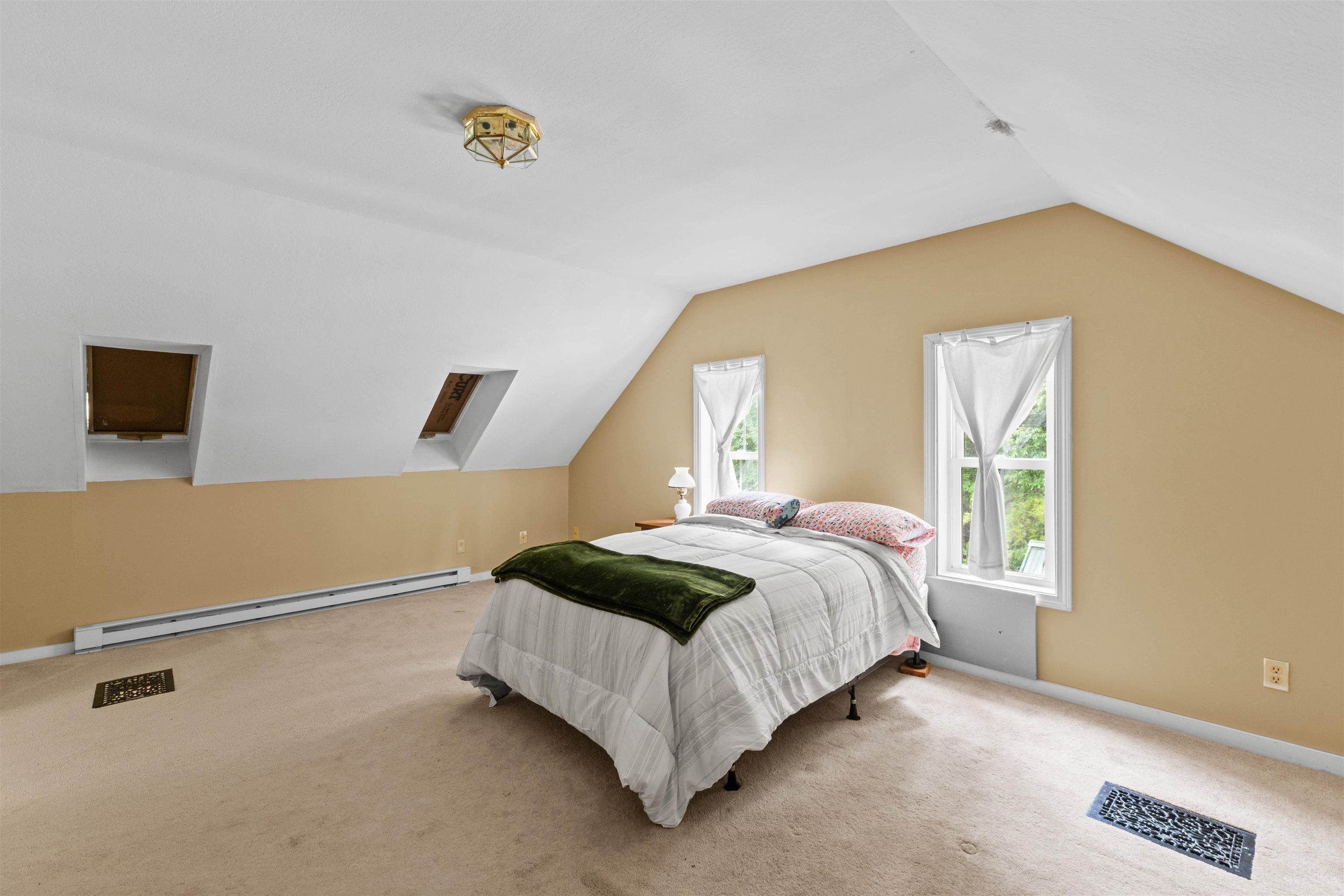 Furnished bedroom with a bed beneath a sloped ceiling and tall curtained windows.