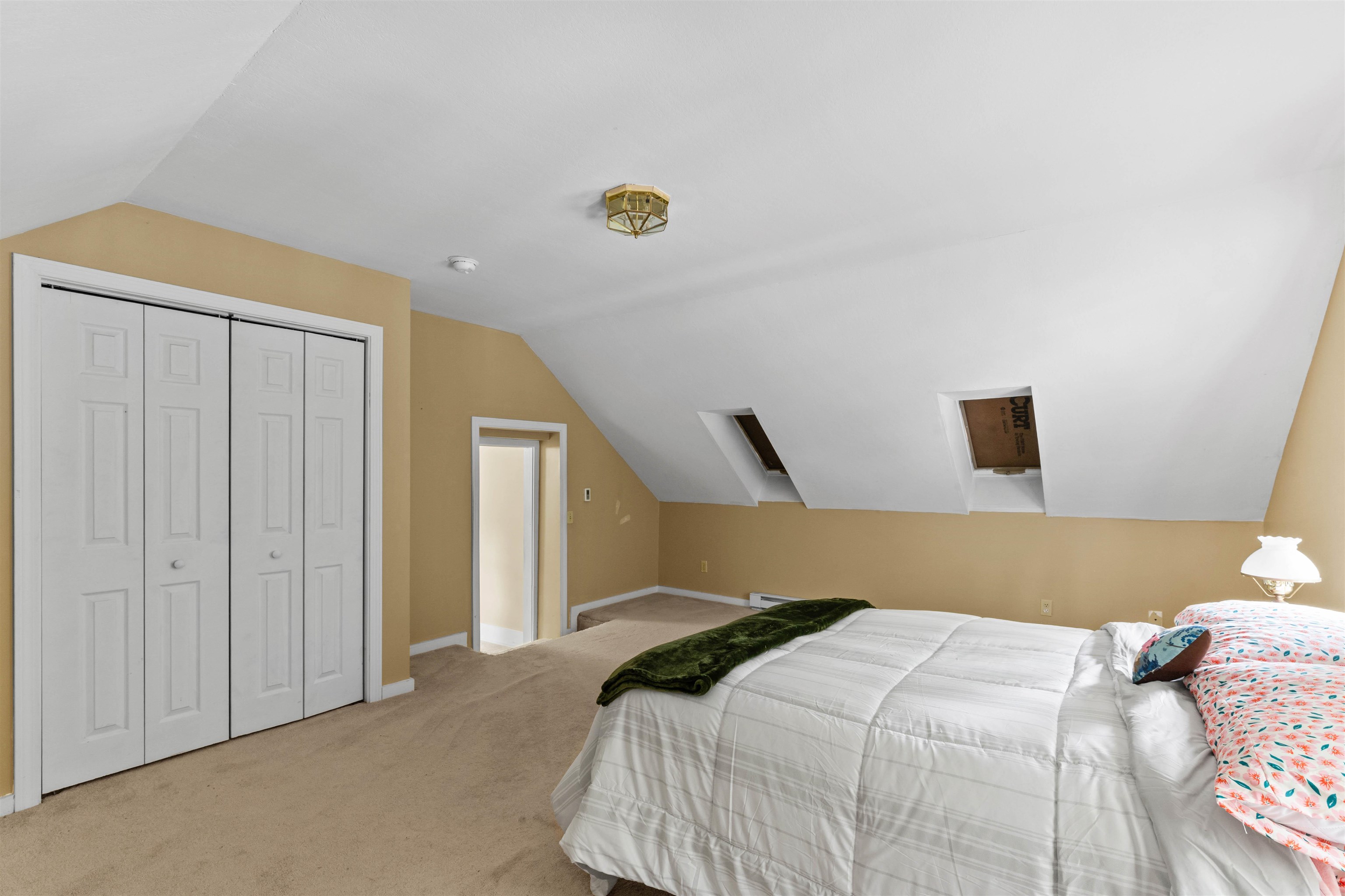 Attic bedroom with a sloped ceiling, two skylights, closet, and bed.