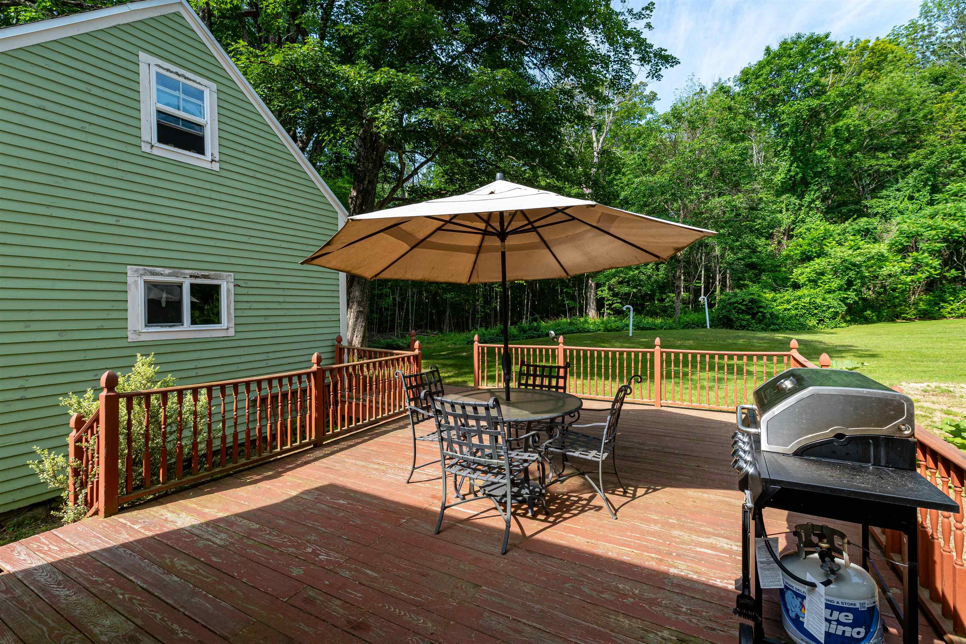 Wooden deck beside a green house, with umbrella-shaded patio furniture and a gas grill.