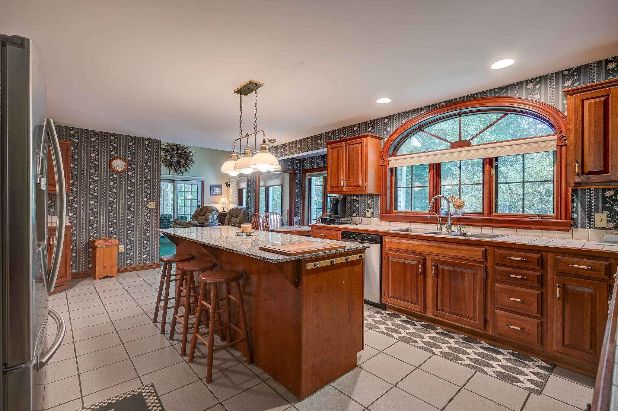 Kitchen with a granite island, cherry cabinets, and a large arched window.