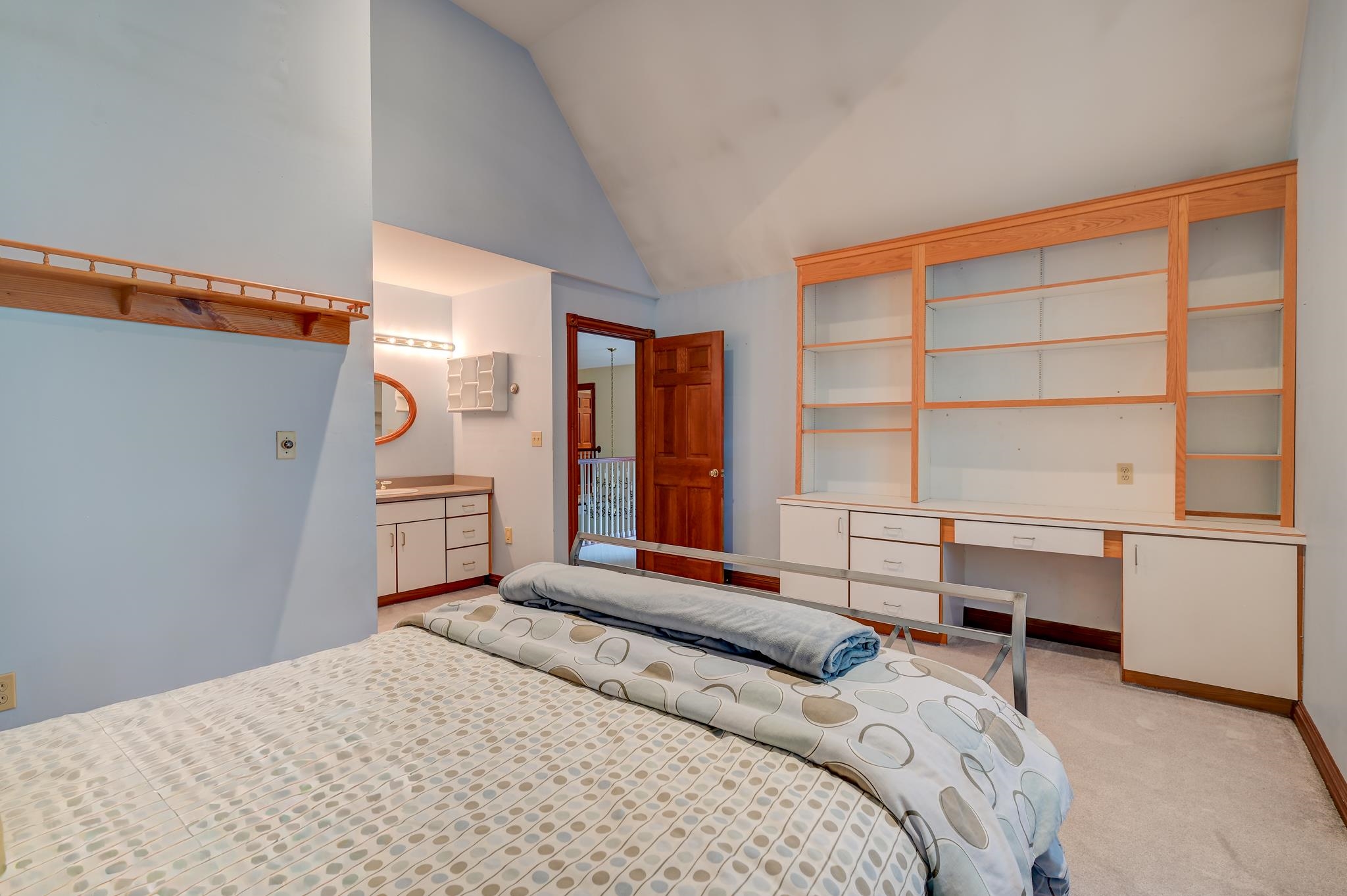 Bedroom with a patterned bed, vaulted ceiling, and built-in wooden shelving.