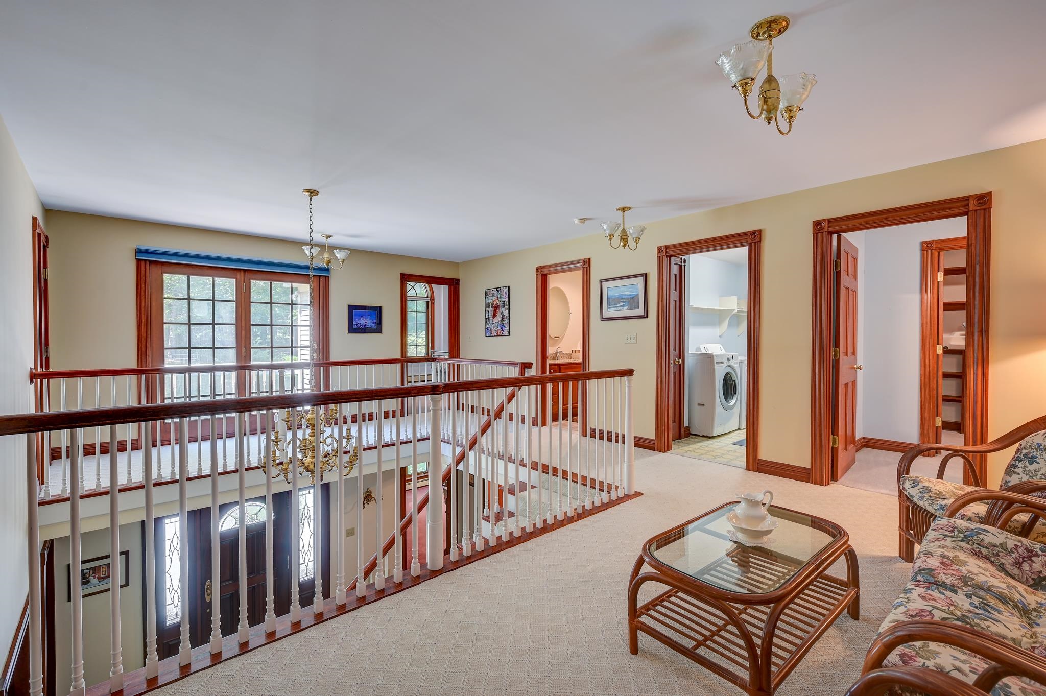 Upstairs landing with a white railing, wood-trimmed doorways, and a wicker seating area.